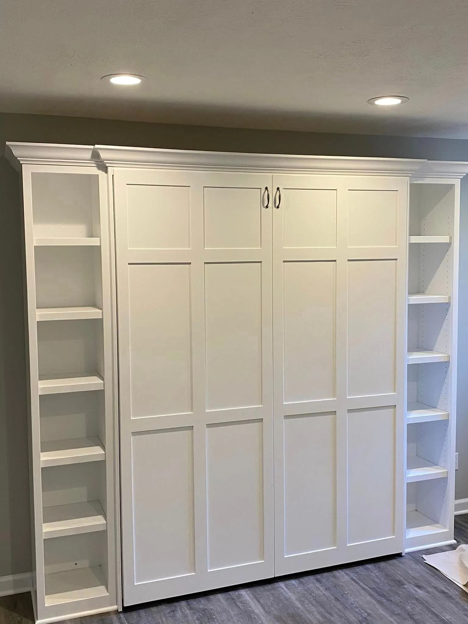 Built-in white closet cabinetry with shelves and central paneled doors under recessed ceiling lights