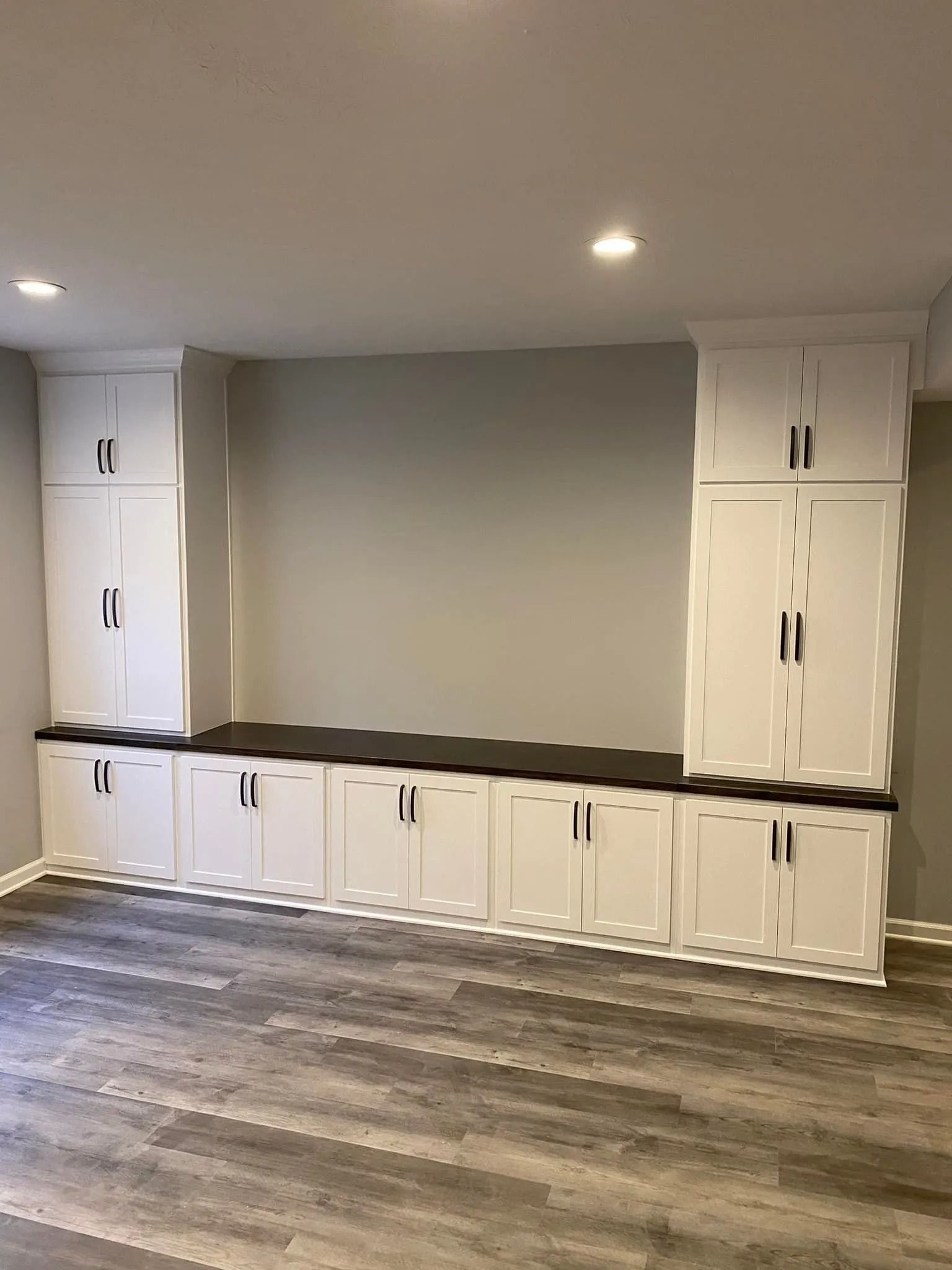 Built-in white cabinets and drawers along a gray wall in a modern room with wood flooring and recessed lights