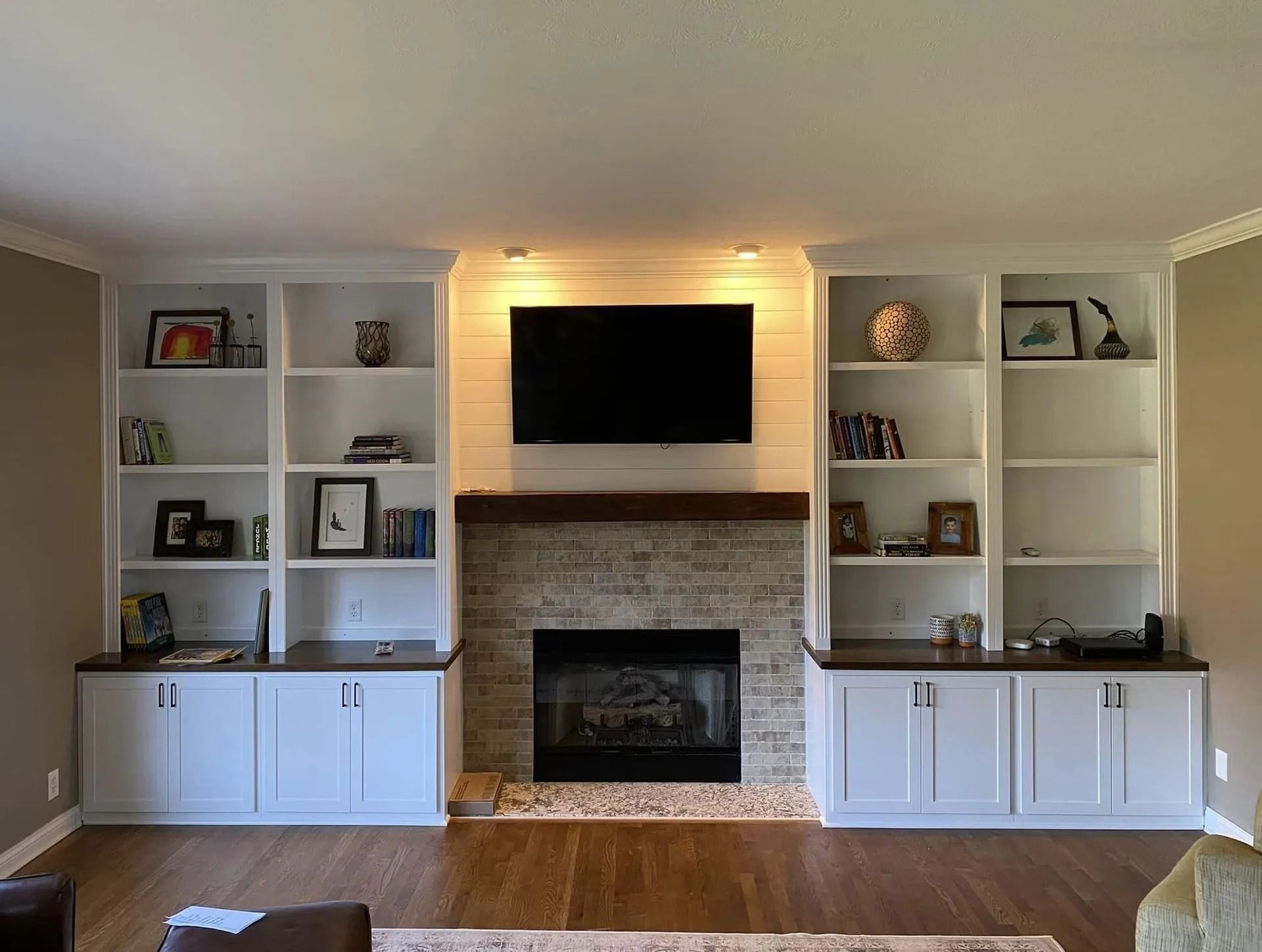 Living room with built-in white shelves, brick fireplace, mounted TV, and hardwood floors
