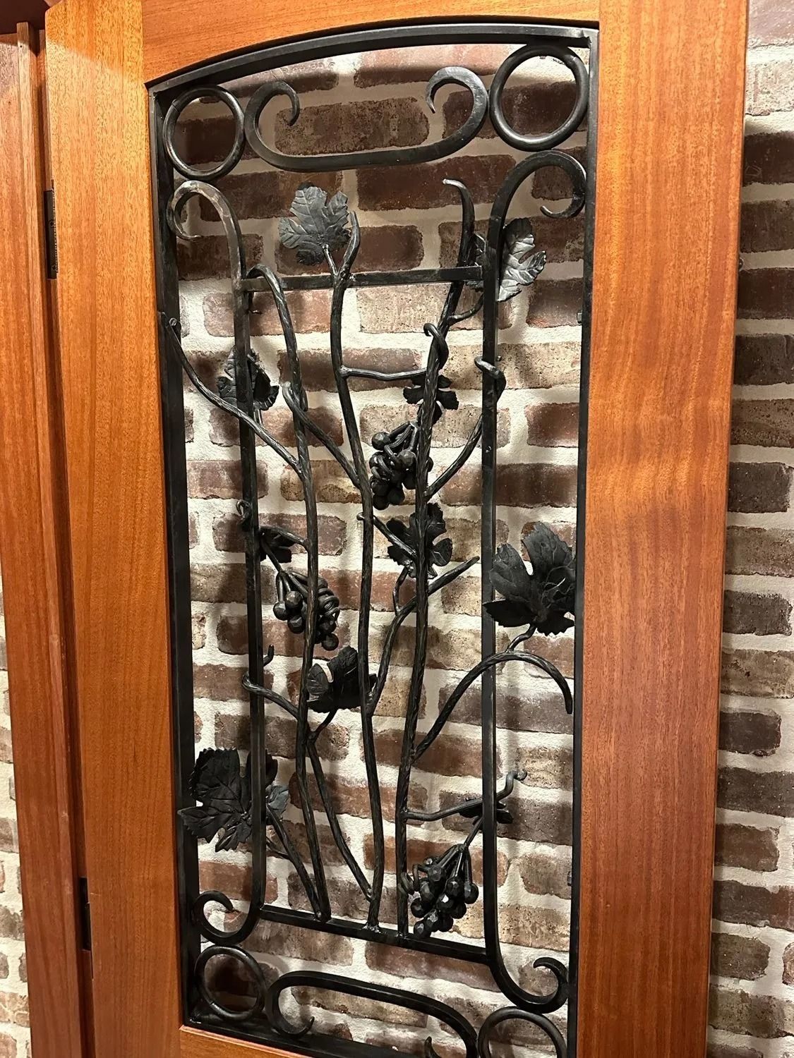 Decorative wrought-iron panel with vine and leaf design set in a wooden door frame
