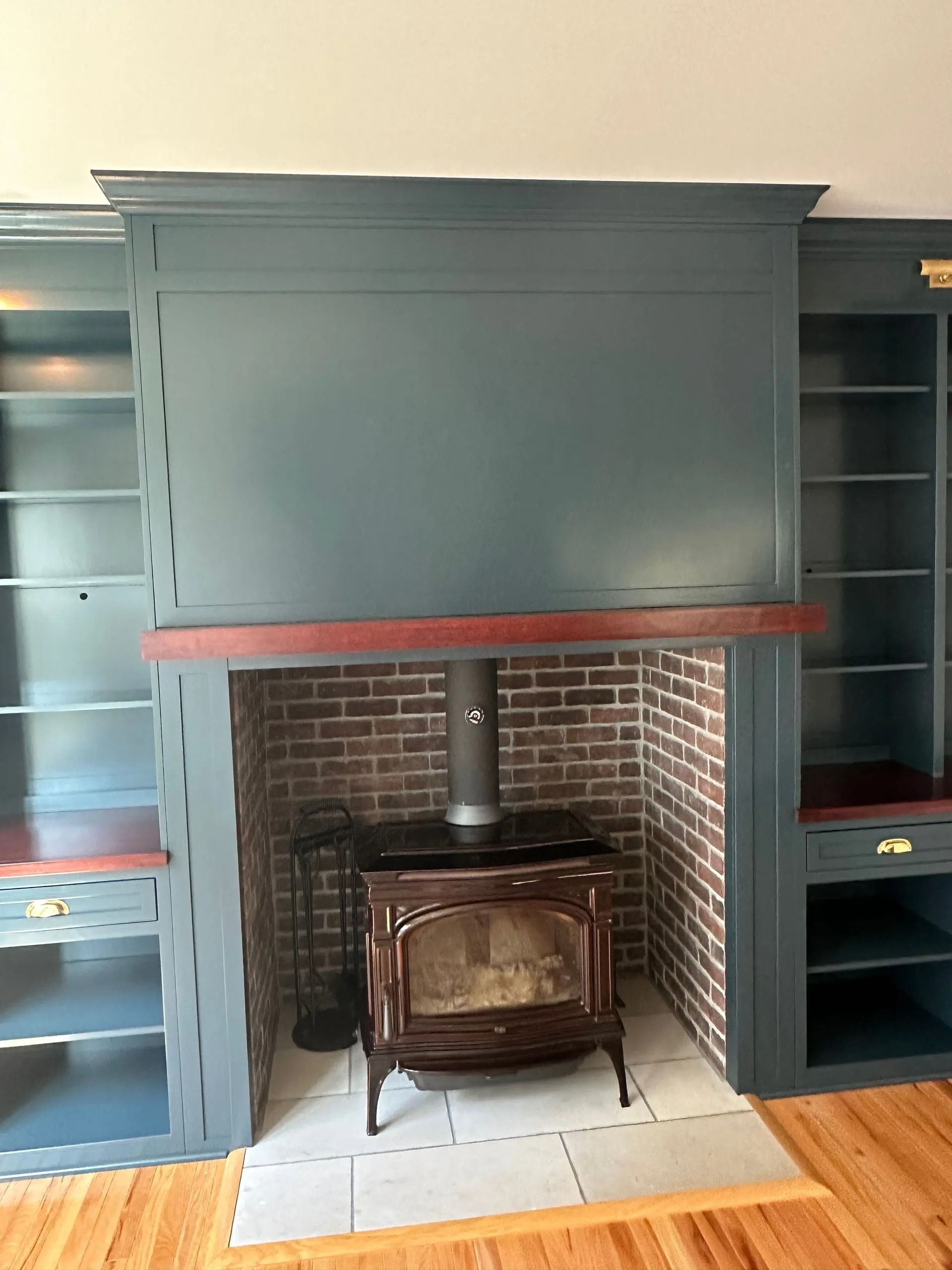Blue built-in shelves flanking a brick fireplace with a wood stove and red mantel on hardwood floor