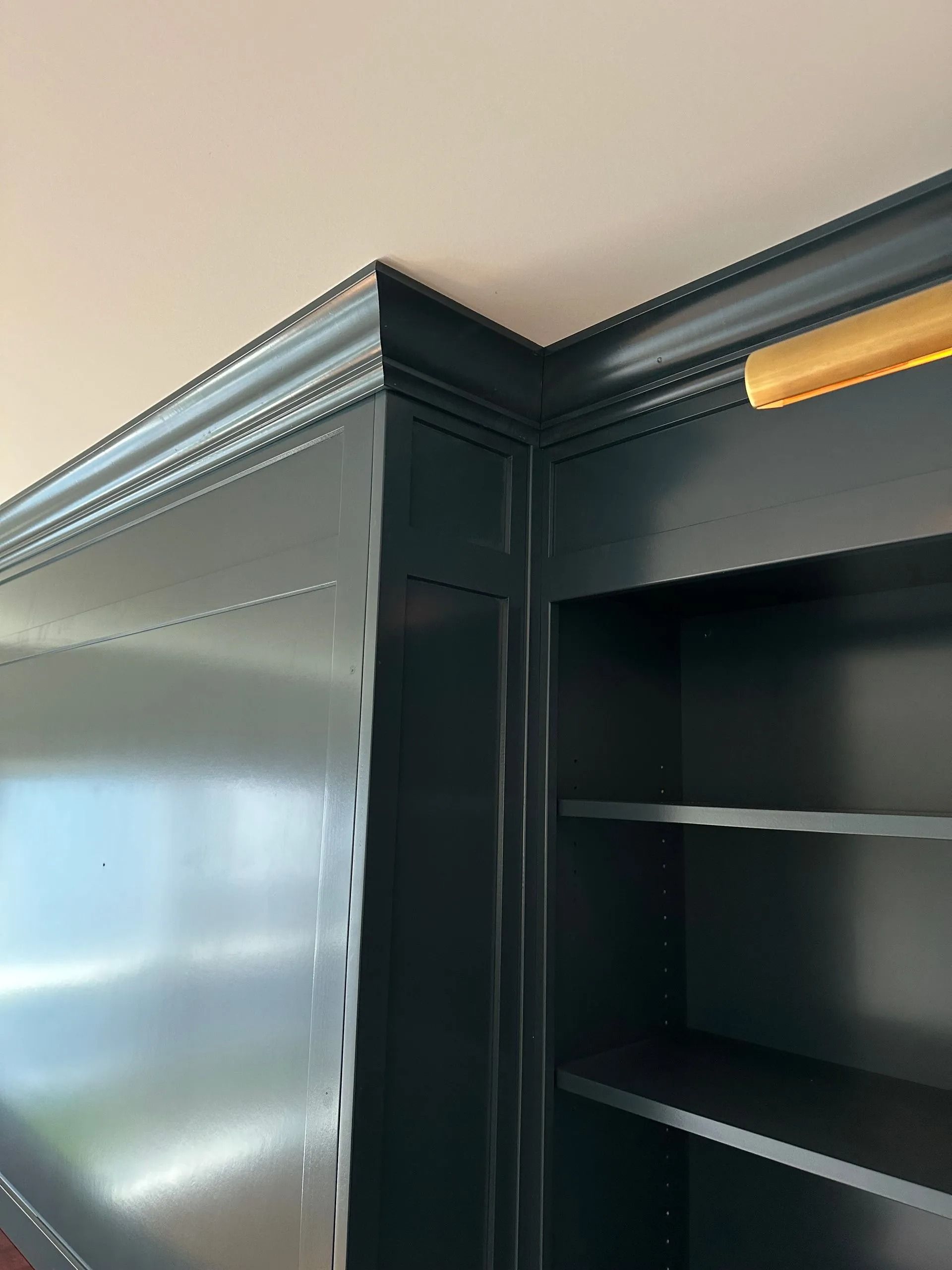 Close-up of a dark green cabinet corner with crown molding and open shelves