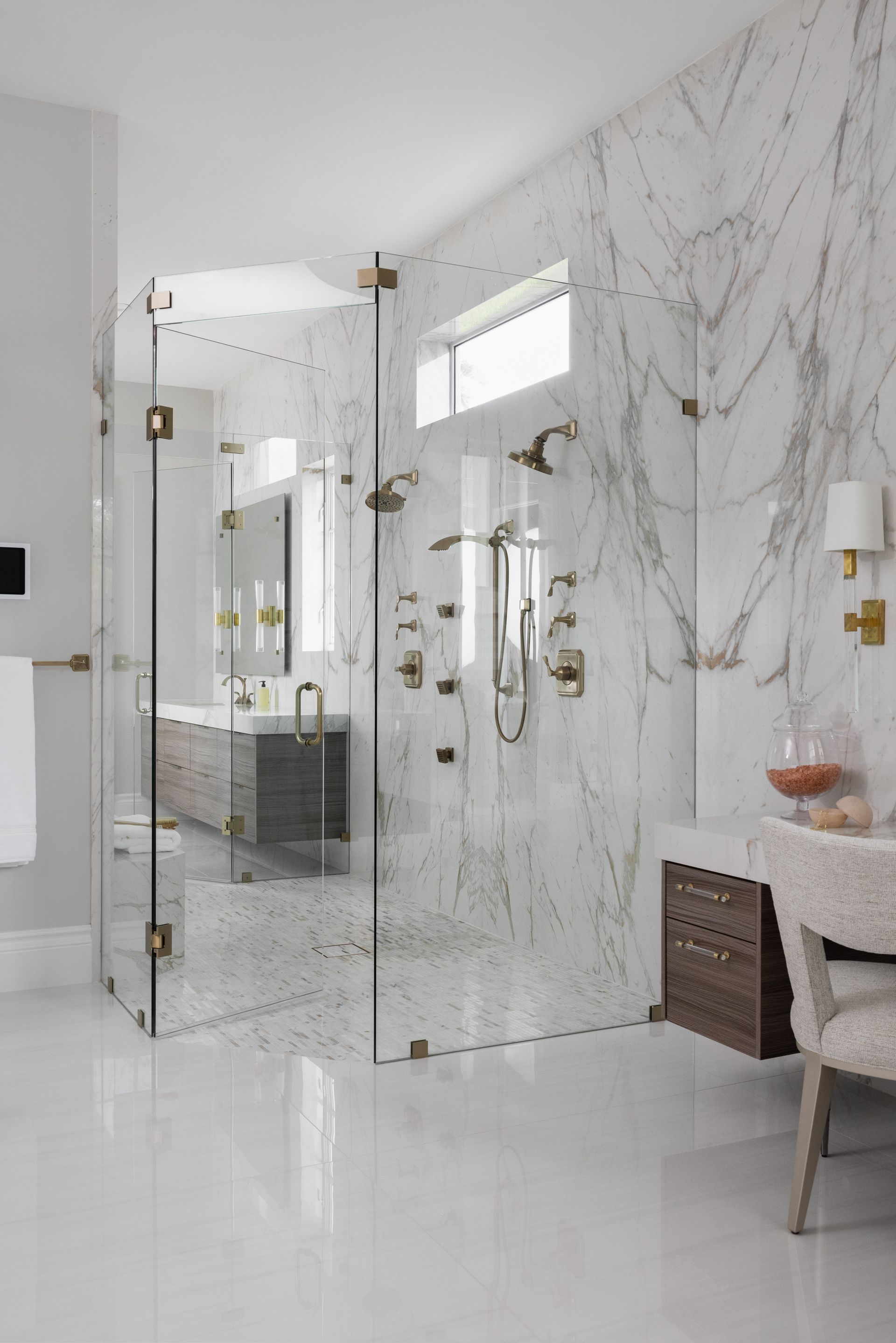 A bathroom with marble walls and a walk-in shower with glass doors.