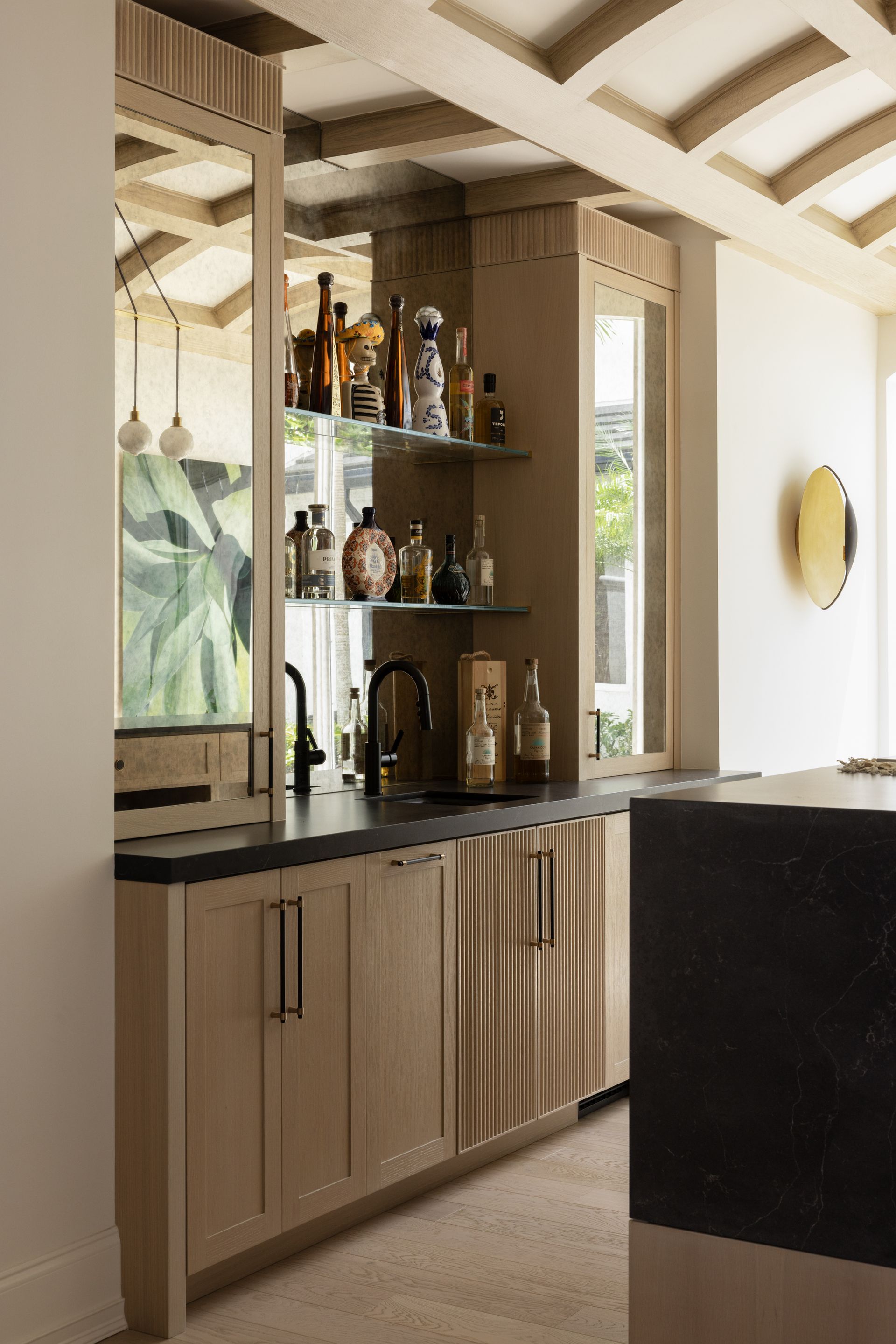 A kitchen with a bar and lots of bottles on shelves.