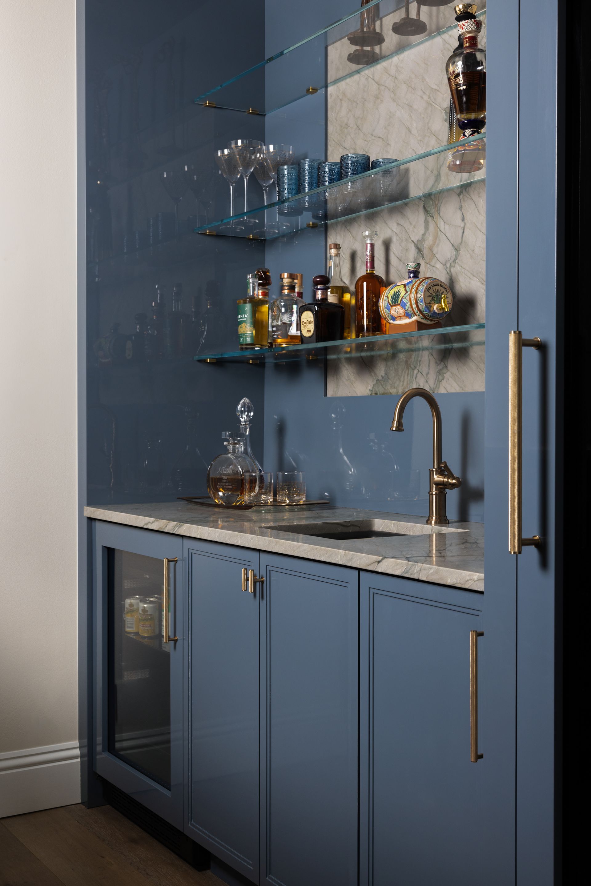 A kitchen with blue cabinets and a bar with bottles and glasses on shelves.