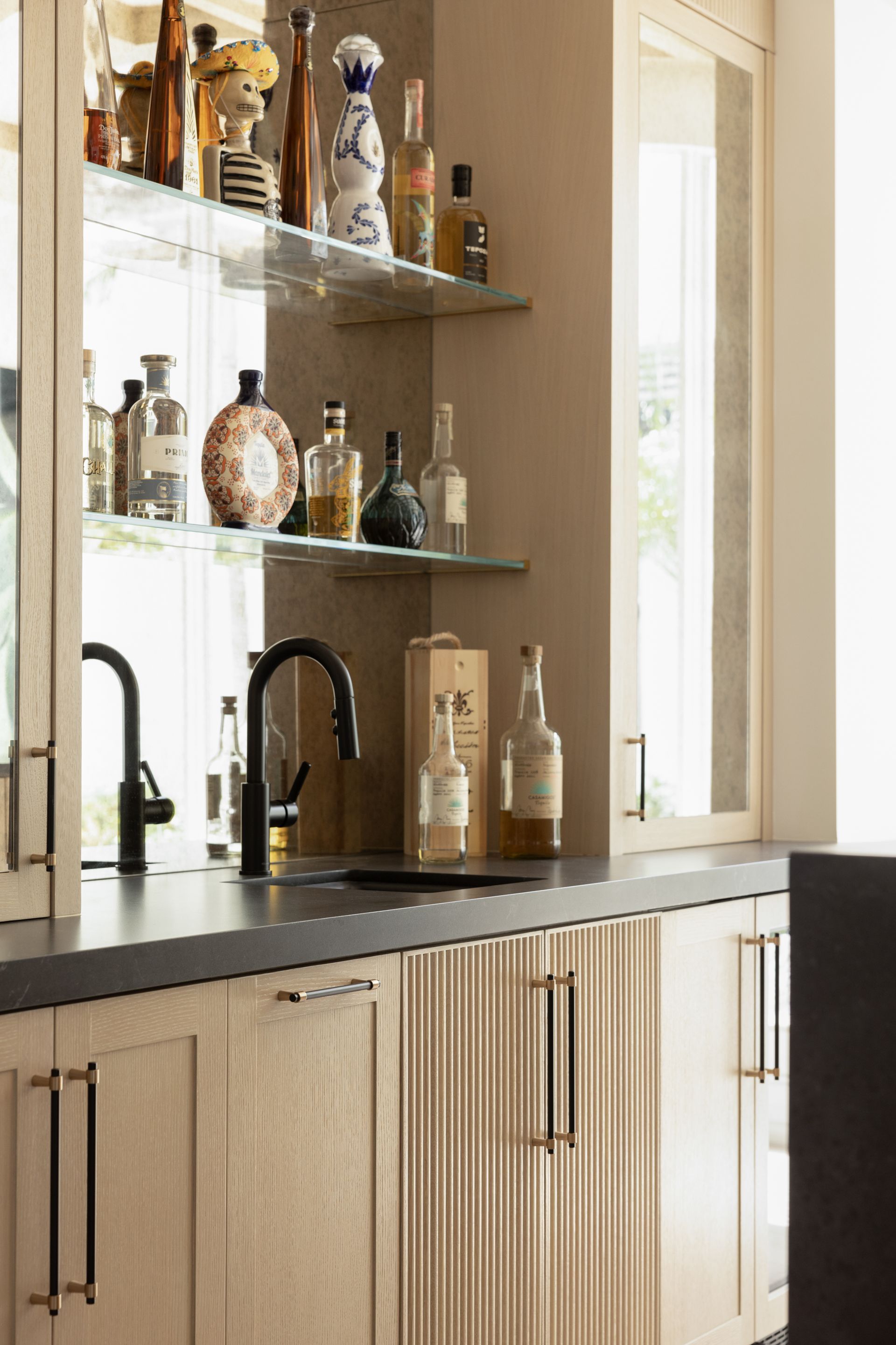 A kitchen with a sink and a bar with bottles on shelves.