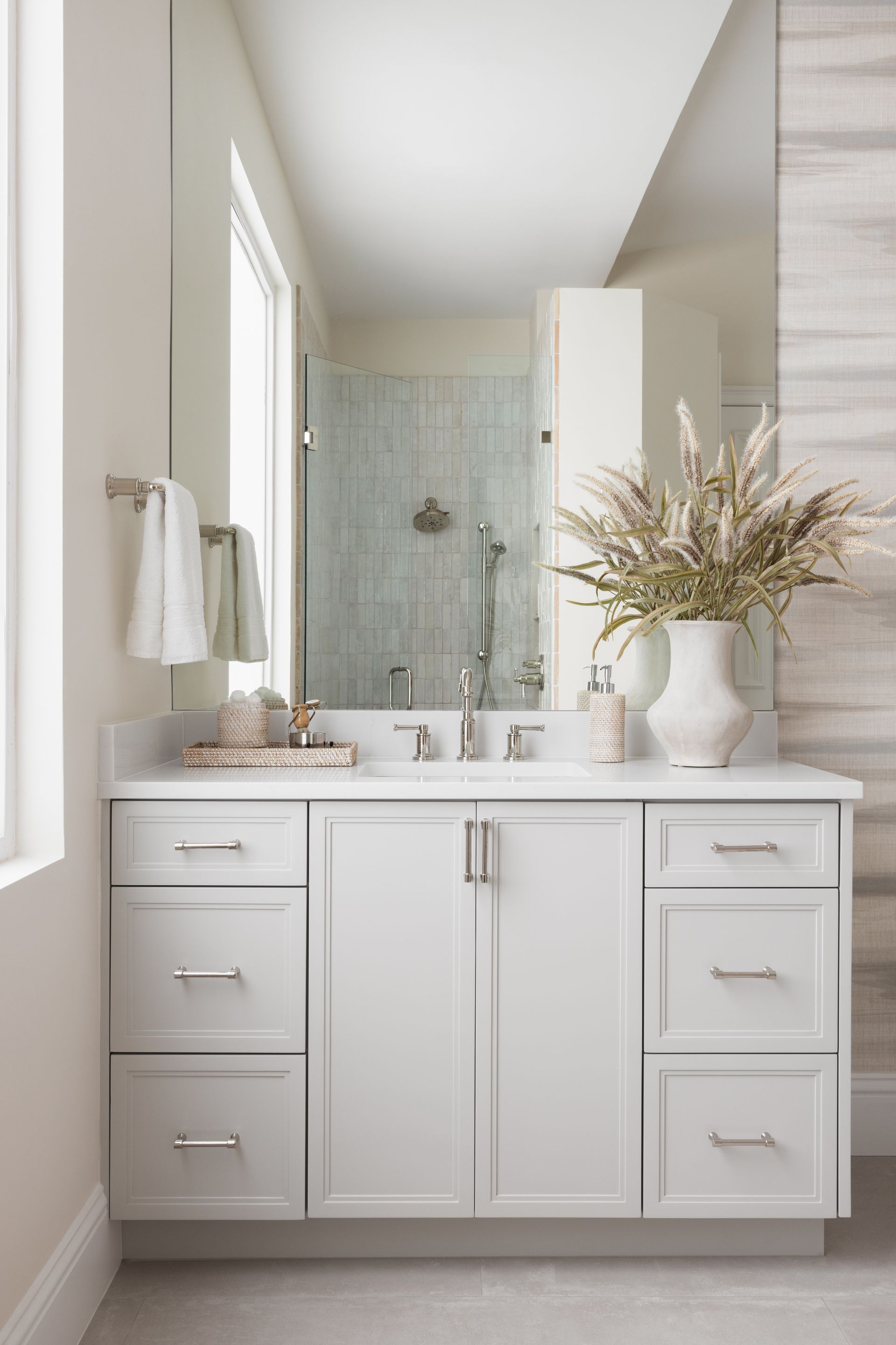 A bathroom with white cabinets, drawers, a sink and a mirror.
