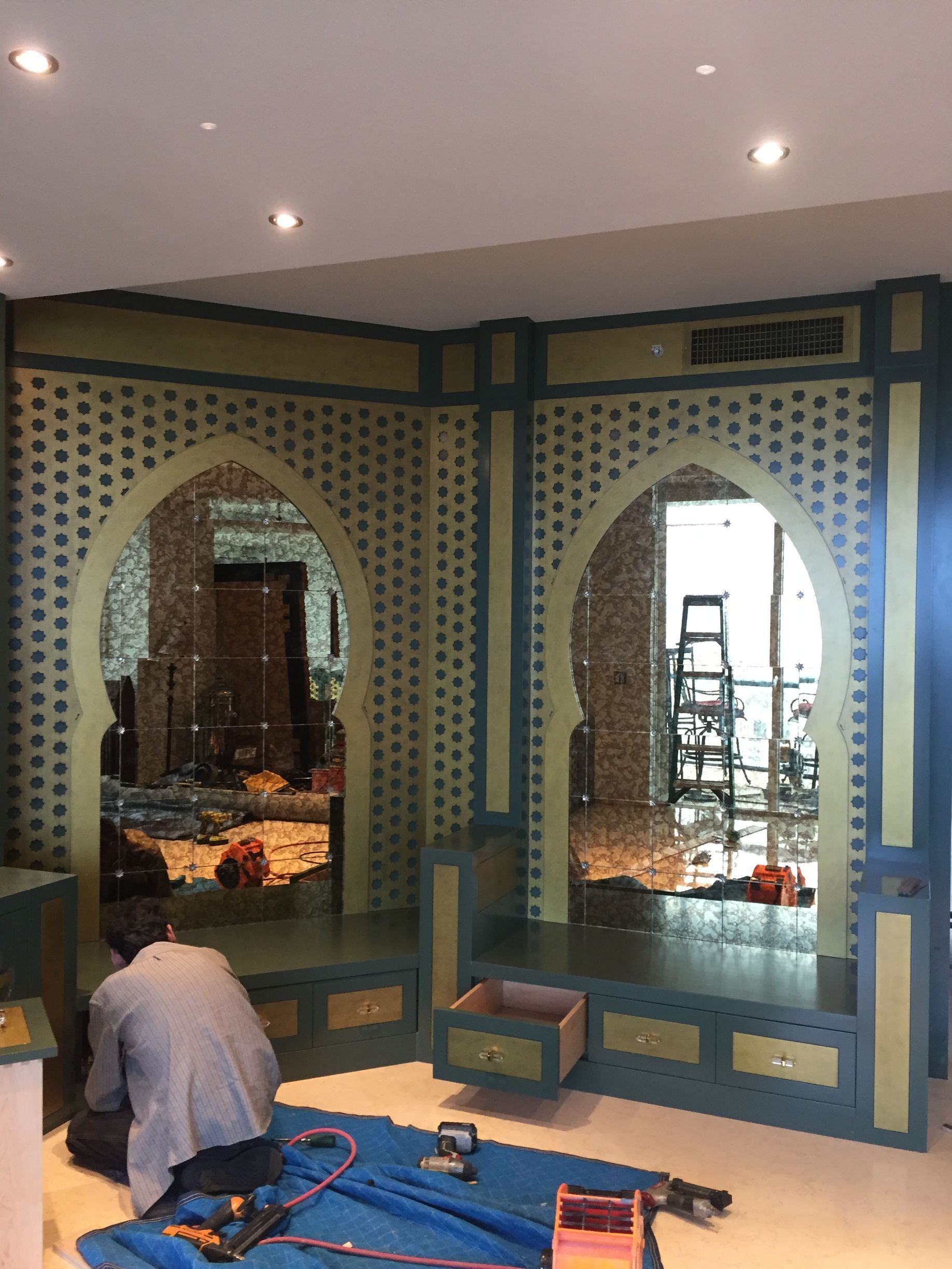 A man is kneeling on the floor in front of a mirror in a room.