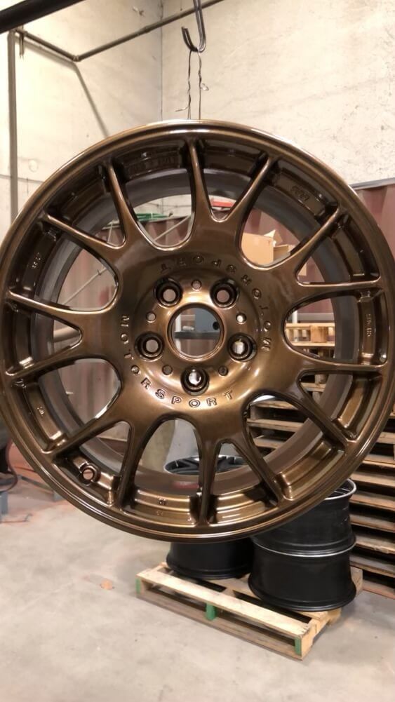 Bronze-colored car wheel, likely recently painted, hanging in a workshop setting.