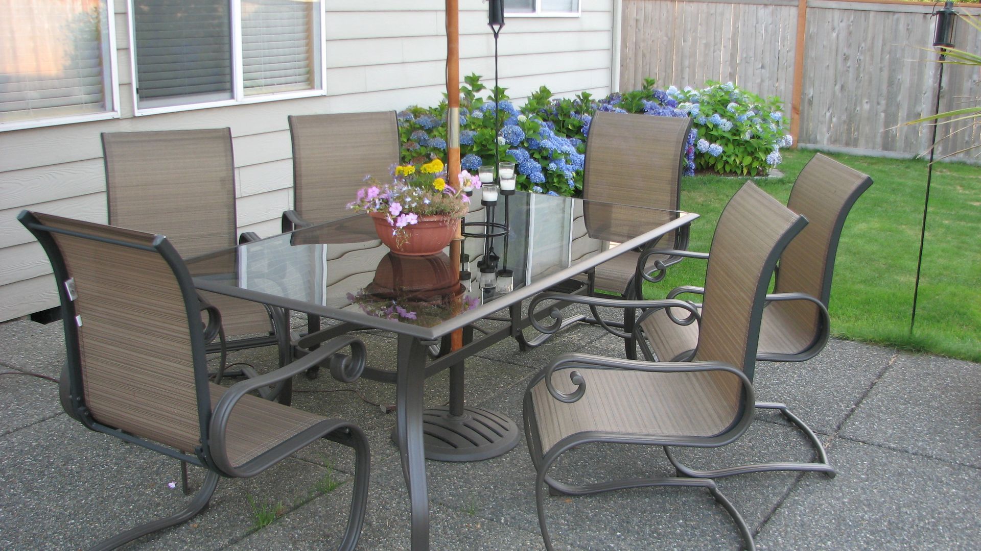 Patio set with six chairs, umbrella, and flowers on a glass-top table.