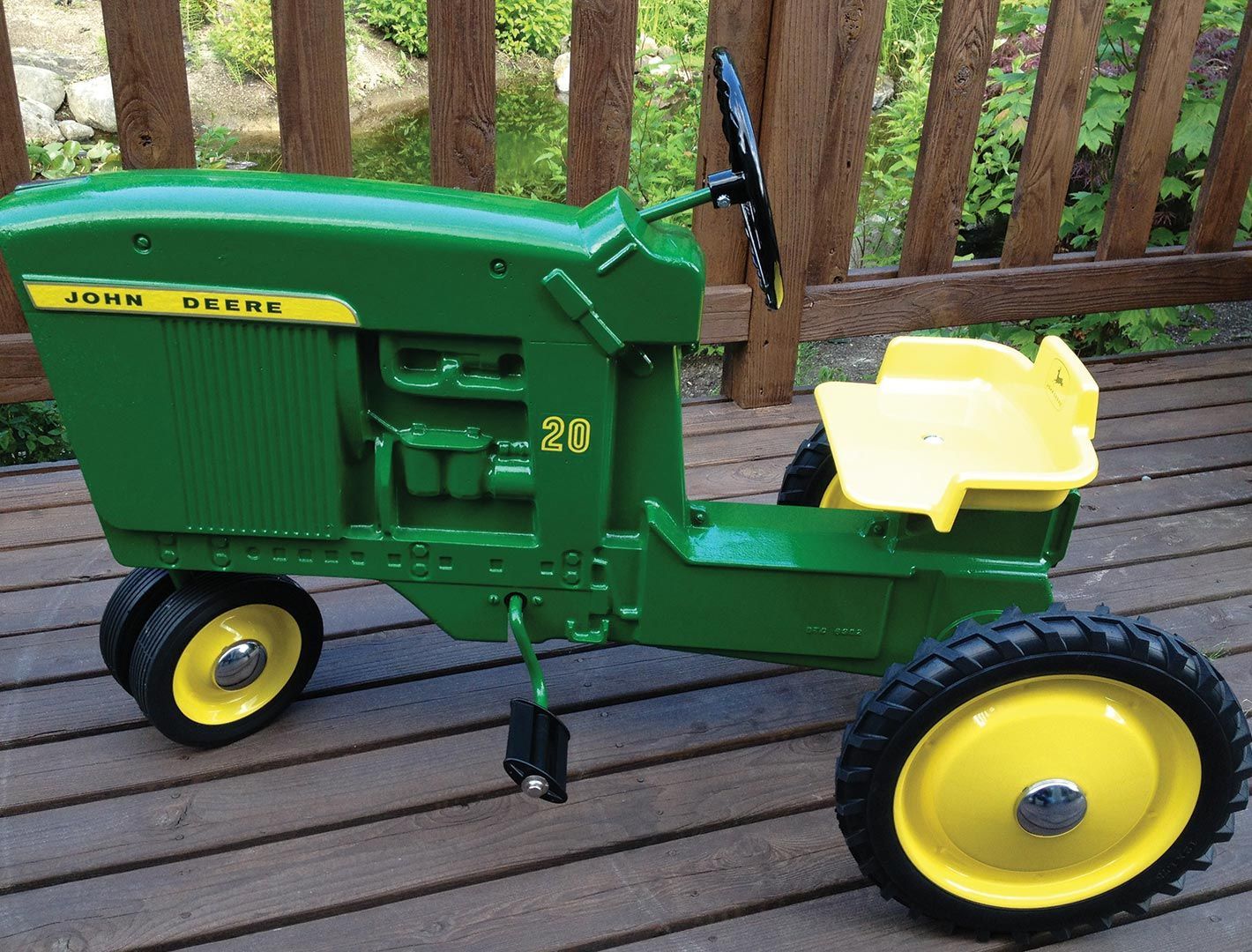 Green and yellow John Deere pedal tractor with black steering wheel and seat.