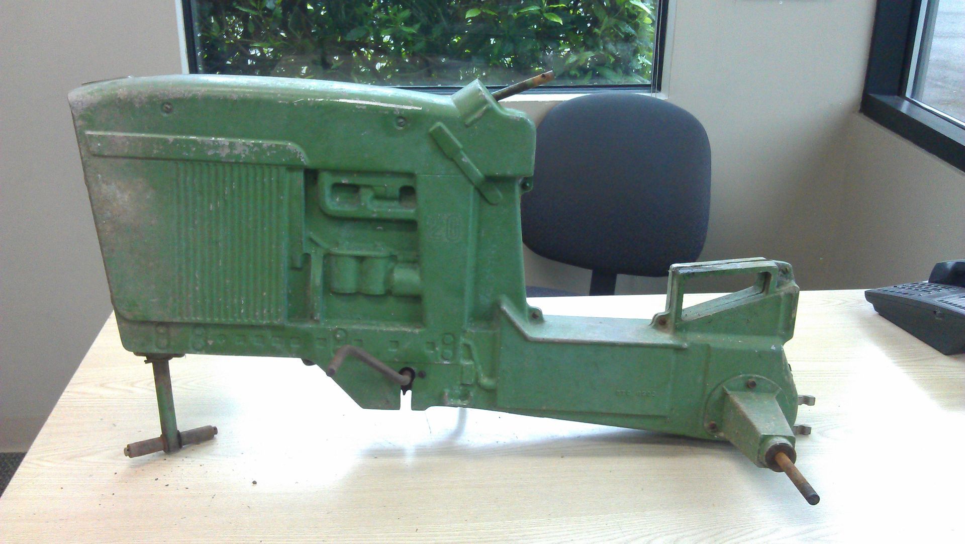 Green toy tractor on a light-colored table. The background includes a window, a chair, and a keyboard.