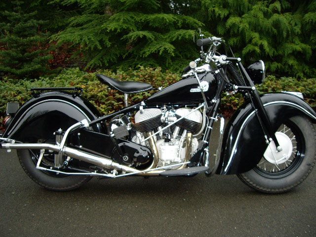 Black vintage Indian motorcycle parked outdoors on wet pavement.