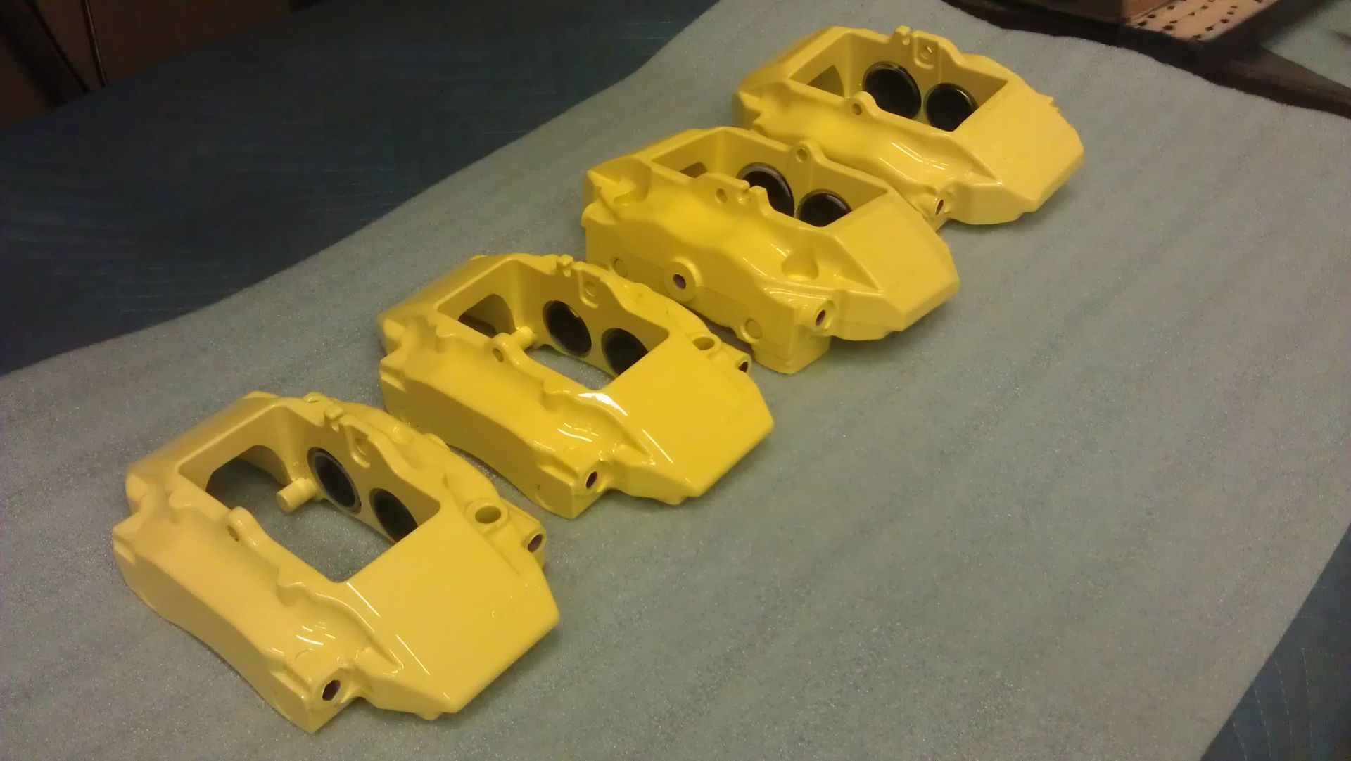 Four yellow car brake calipers on a blue surface, viewed from above.