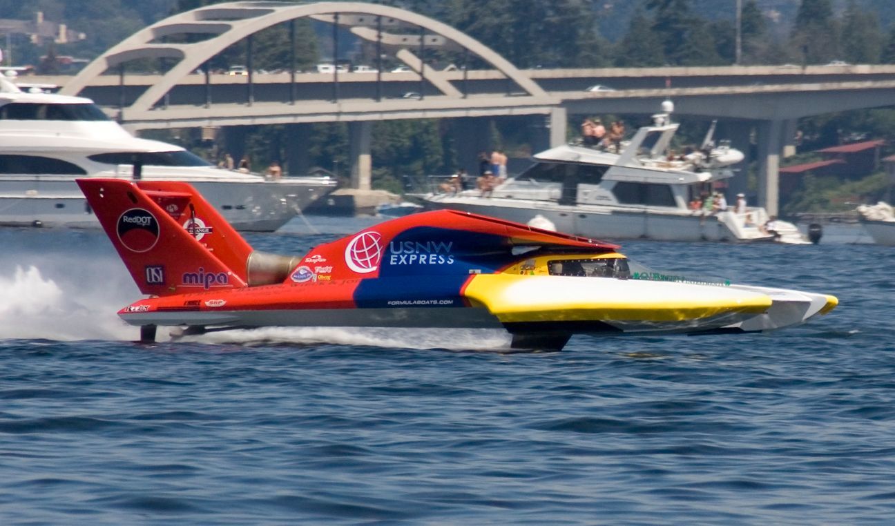 Hydroplane boat, red, blue, and yellow, speeds across water during a race.