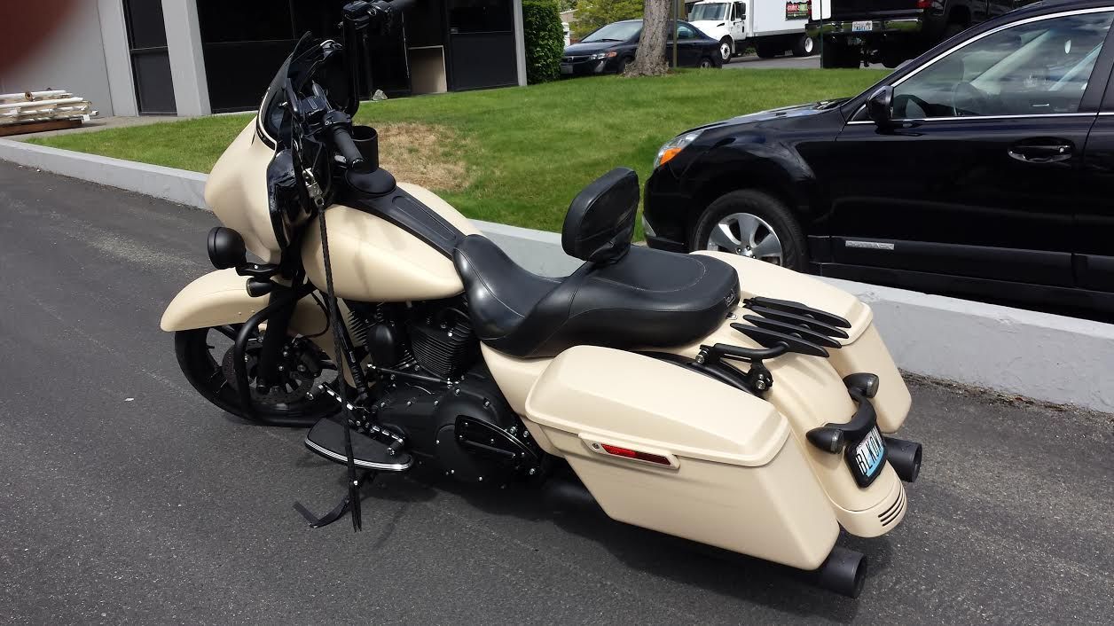 Tan and black motorcycle parked outdoors next to a black car and green grass.