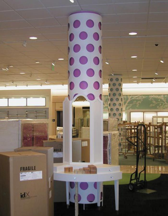 White retail display column with large purple polka dots; white table at its base.