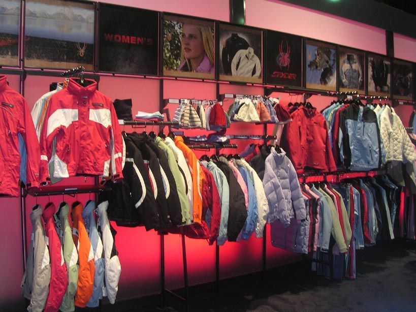 Clothing store display with jackets of various colors, hanging on racks beneath promotional images.