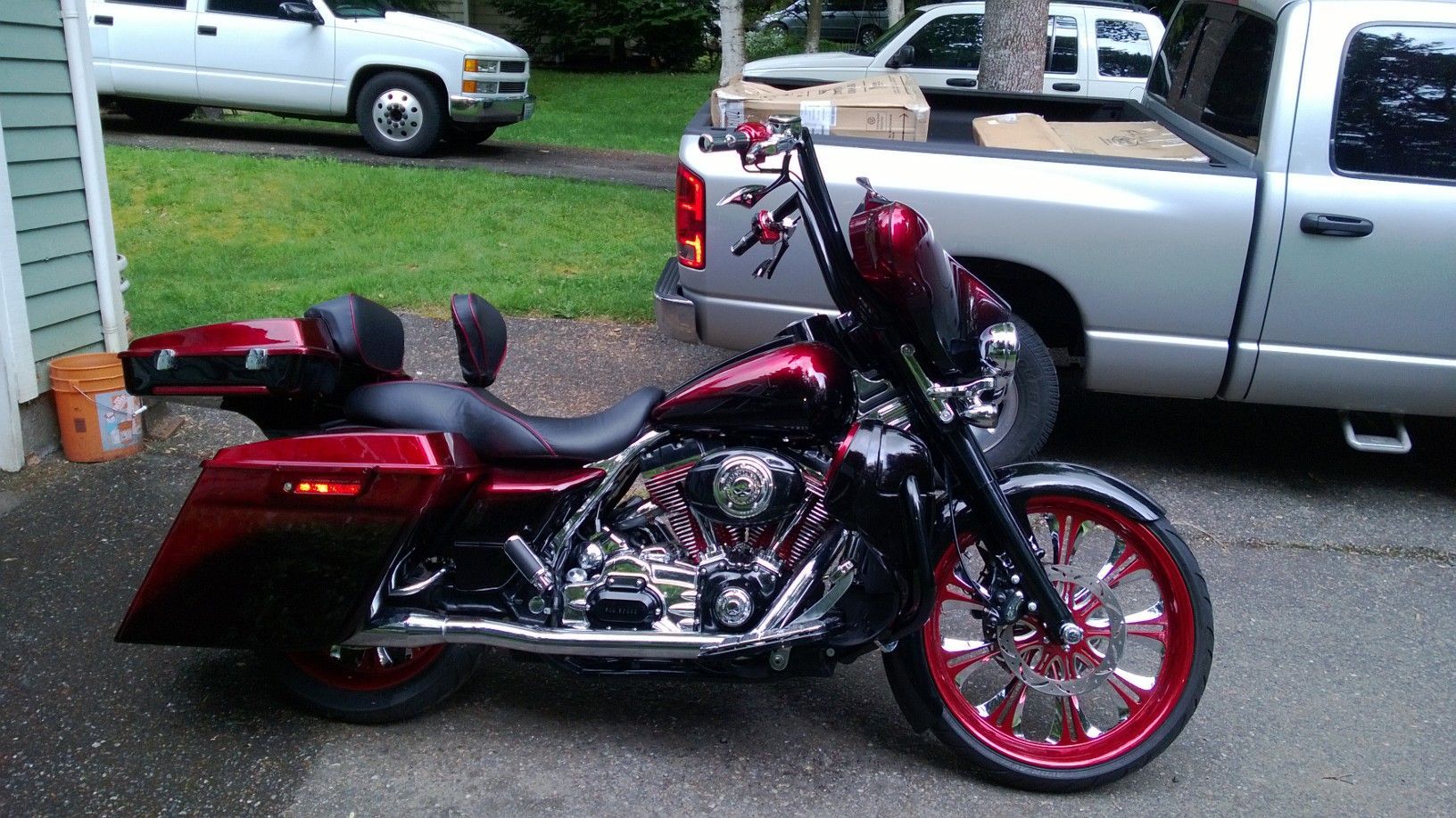 Red and black Harley-Davidson motorcycle with custom wheels parked in front of a white pickup truck on a driveway.