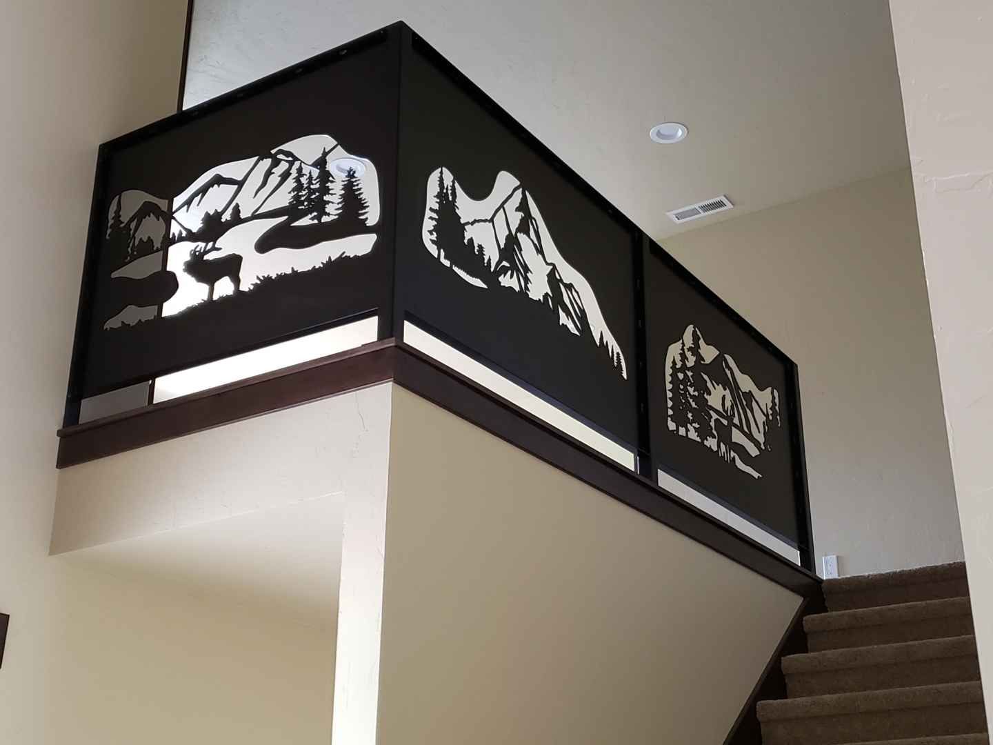Black metal railing with mountain and forest cutouts on a staircase landing.