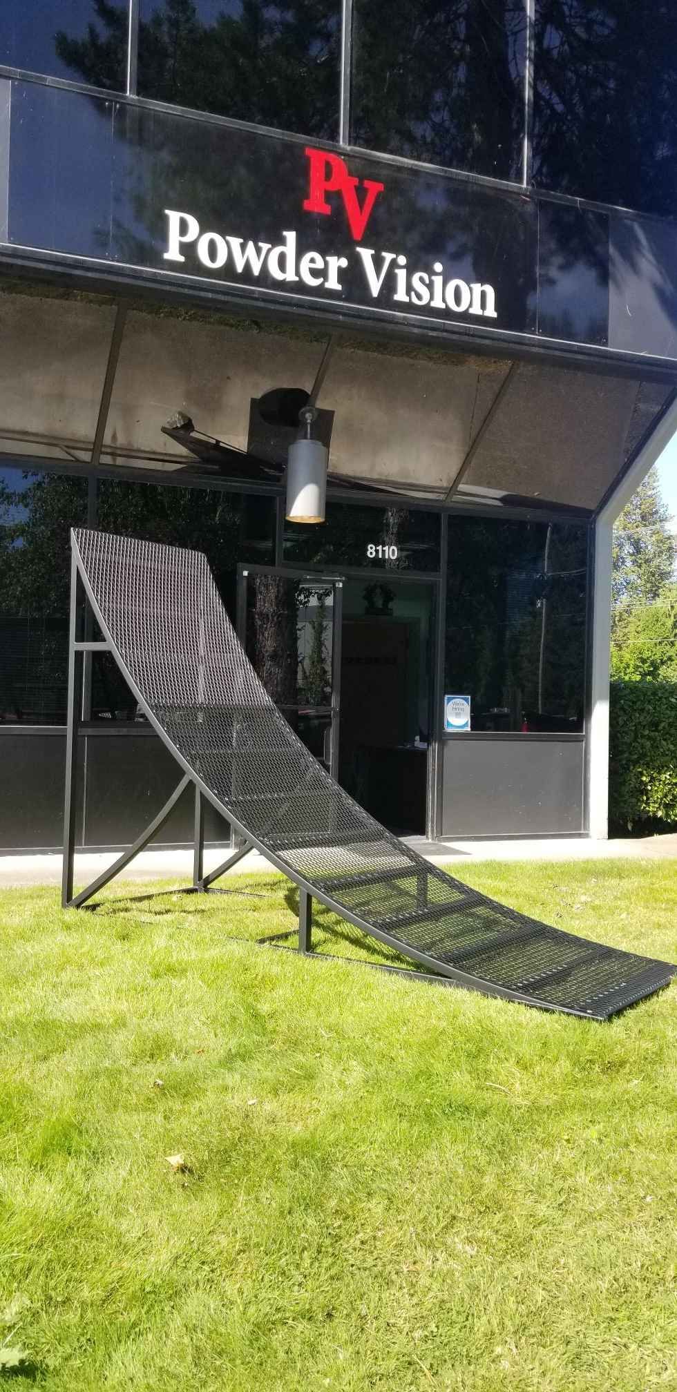 A black metal ramp on a grassy lawn in front of the Powder Vision building.