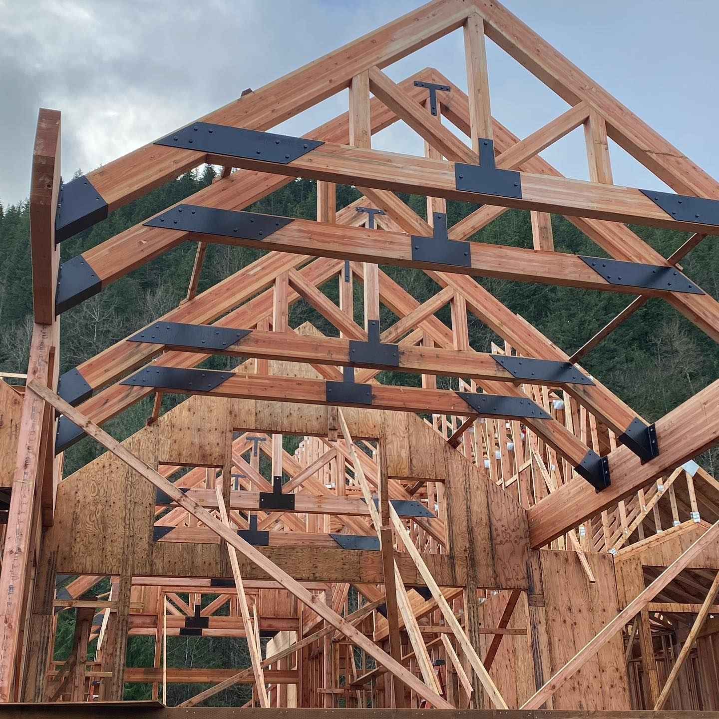 Wooden house frame under construction with exposed beams and trusses, metal connectors.