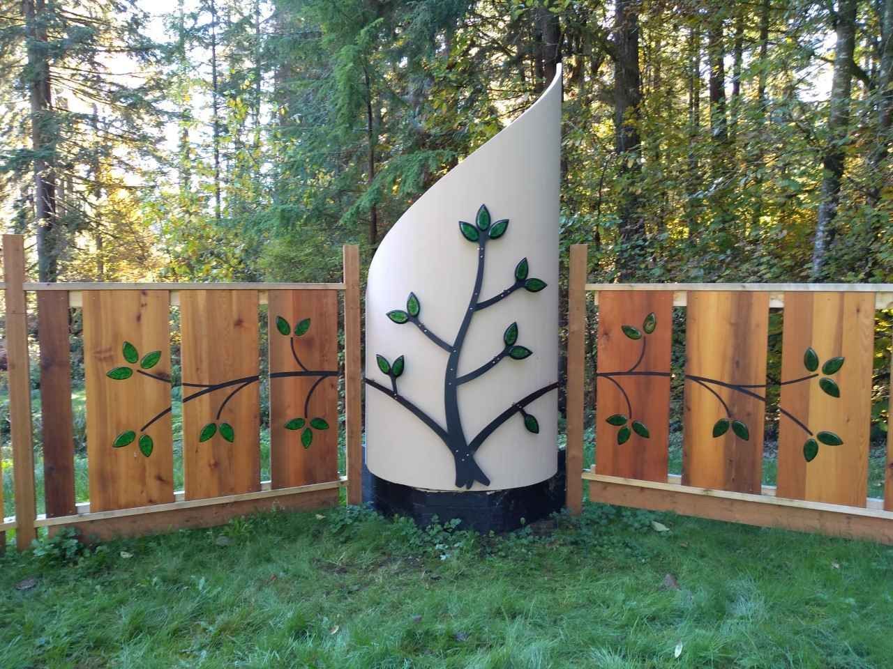 Wooden fence and curved monument with tree silhouette against a backdrop of trees.