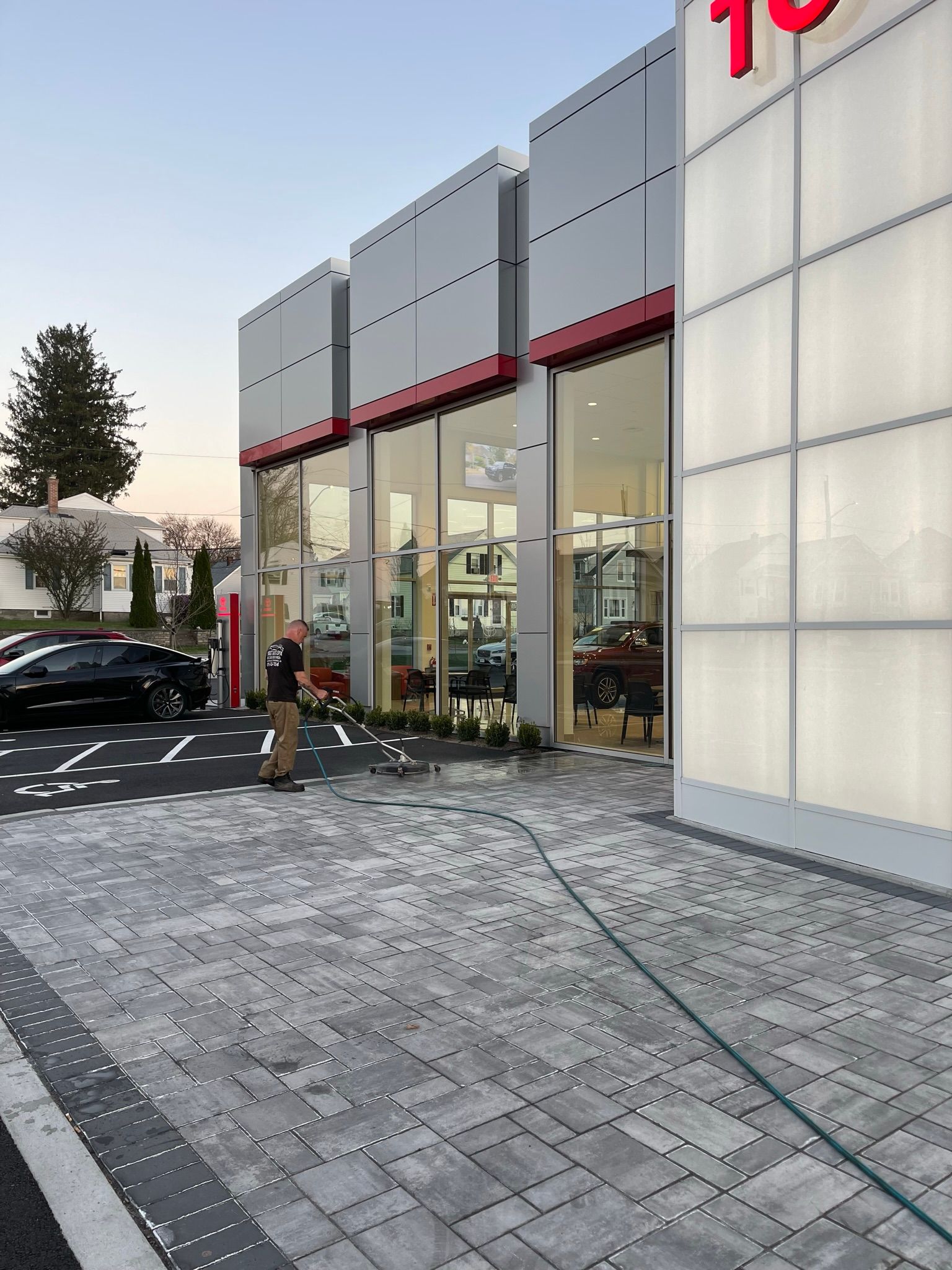 Toyota dealership exterior with glass windows, red trim, and gray paving stones. A person stands near a car.