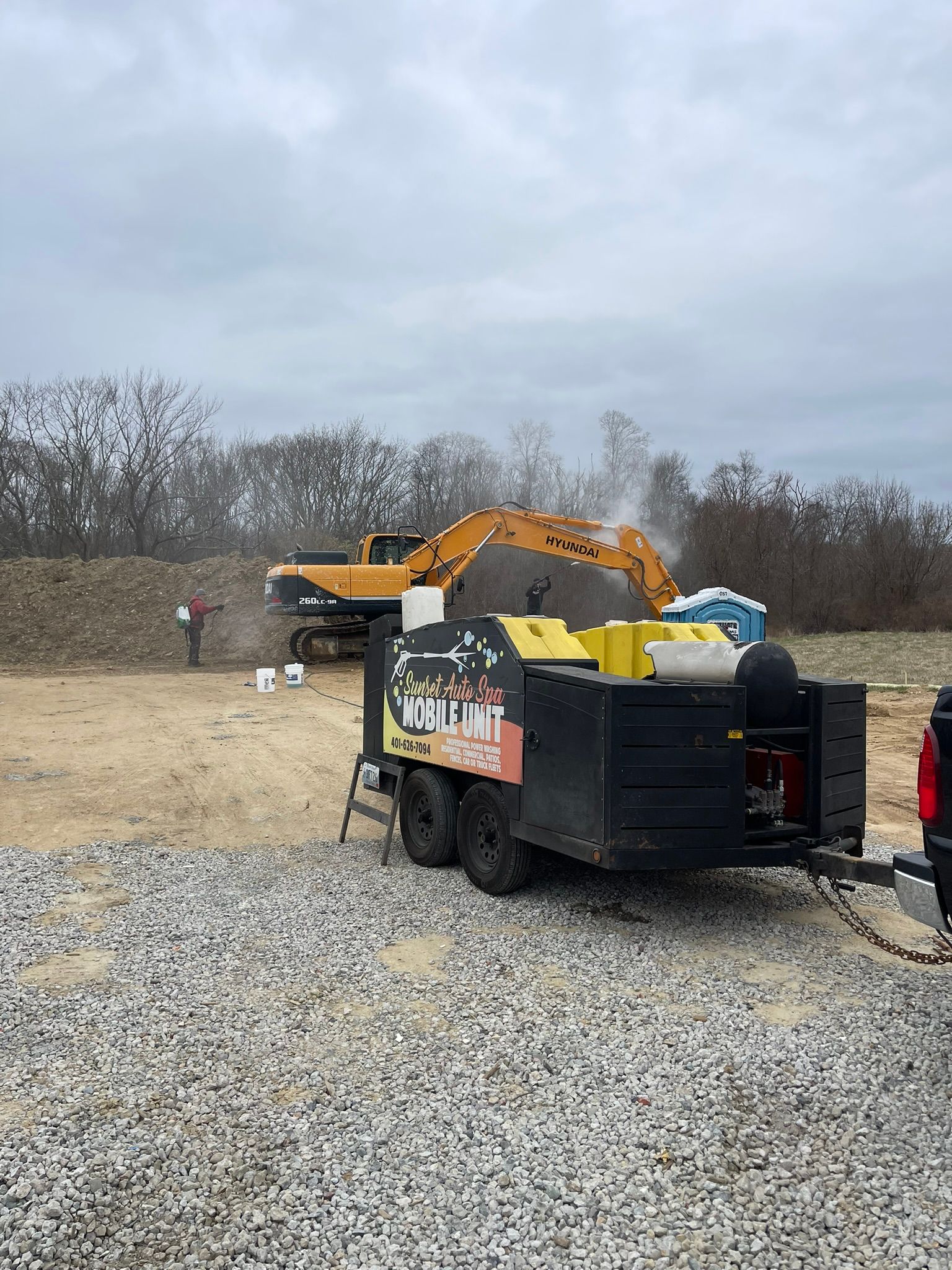 Construction site with excavator and trailer, dust cloud rising.