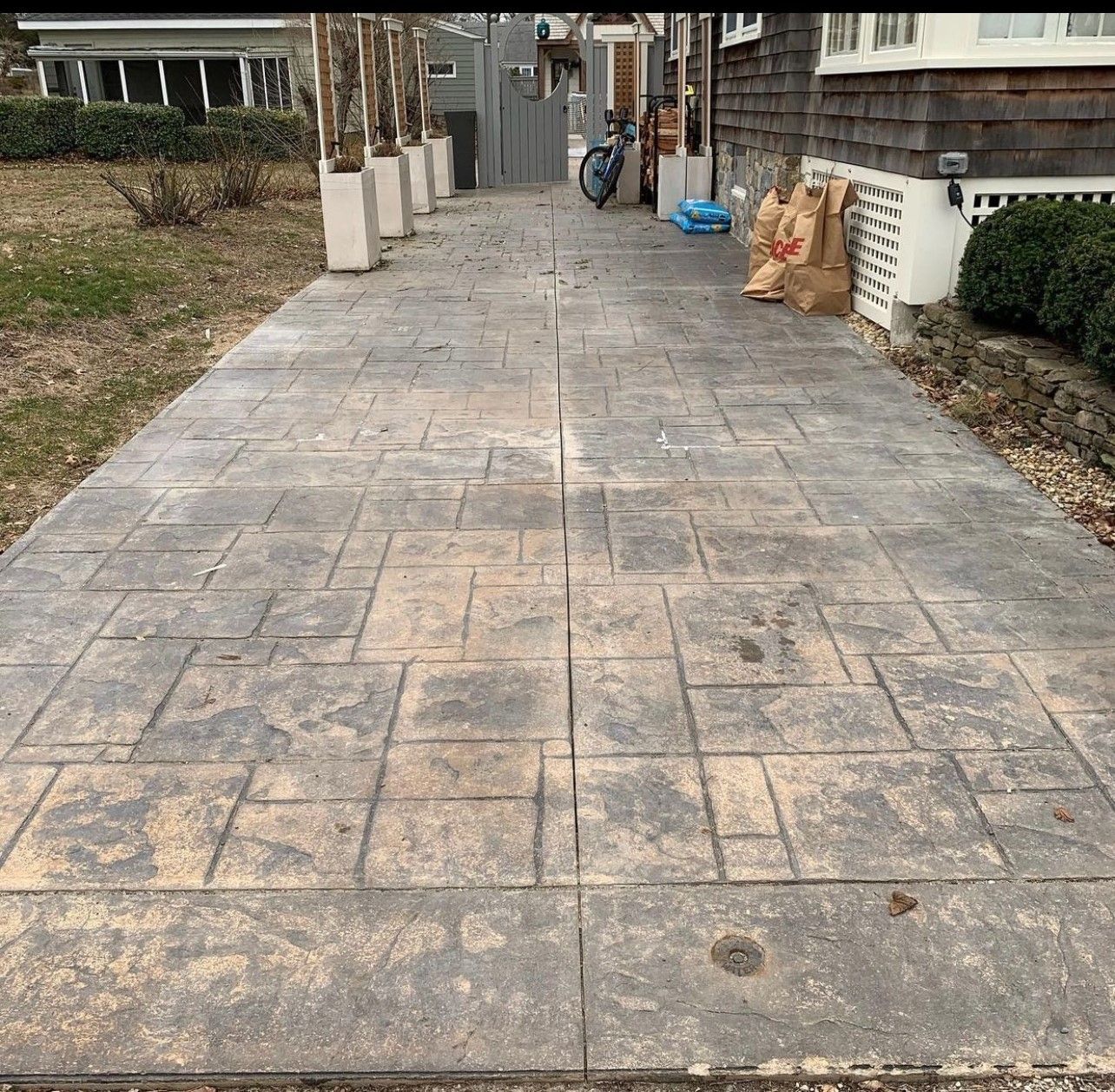 Concrete walkway with patterned squares, leading to a gray gate and house.