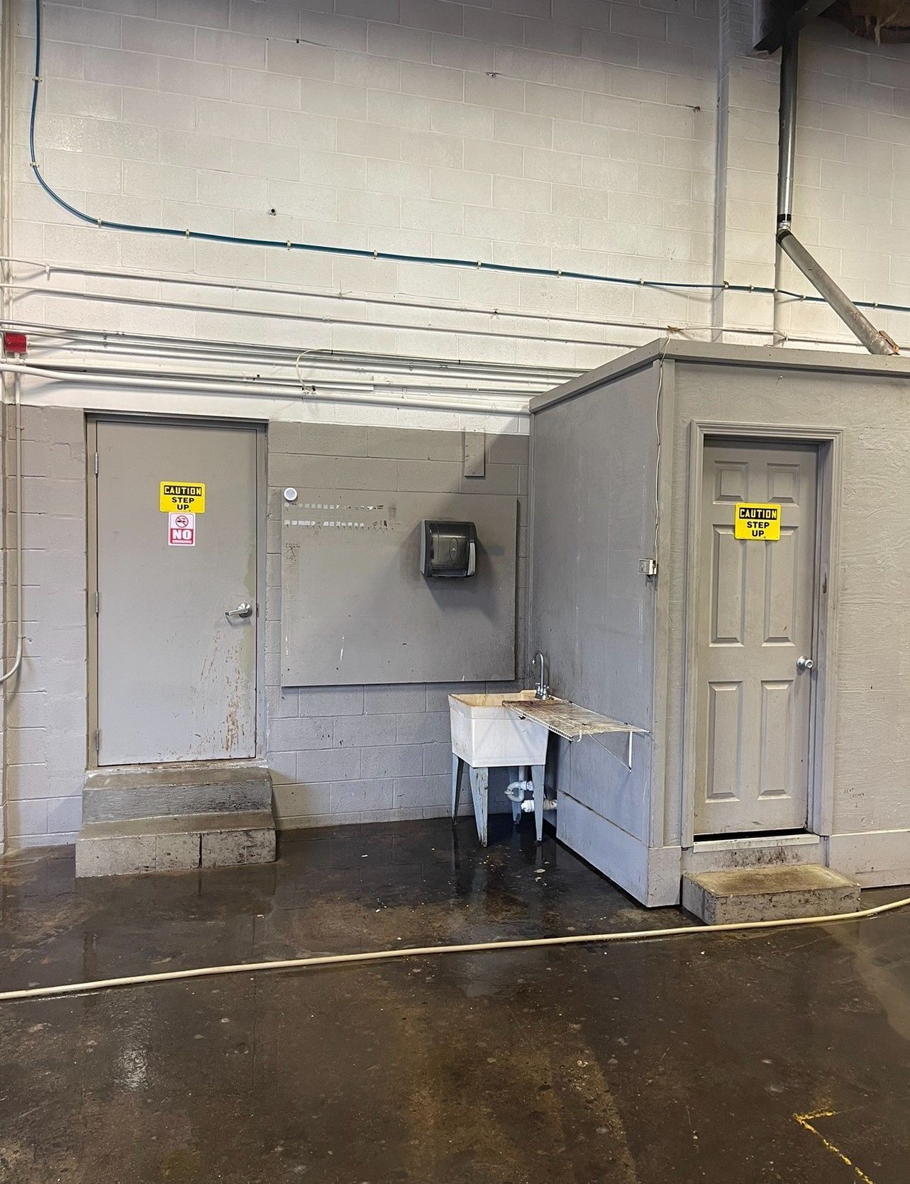 Two gray doors with hazard signs, a sink, and a wall-mounted box in an industrial setting.