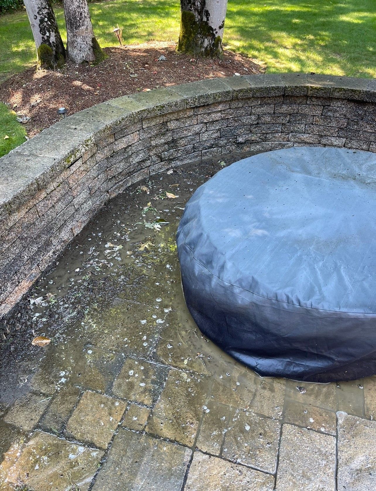 Stone patio with a covered round object and a low stone wall. Trees in the background.
