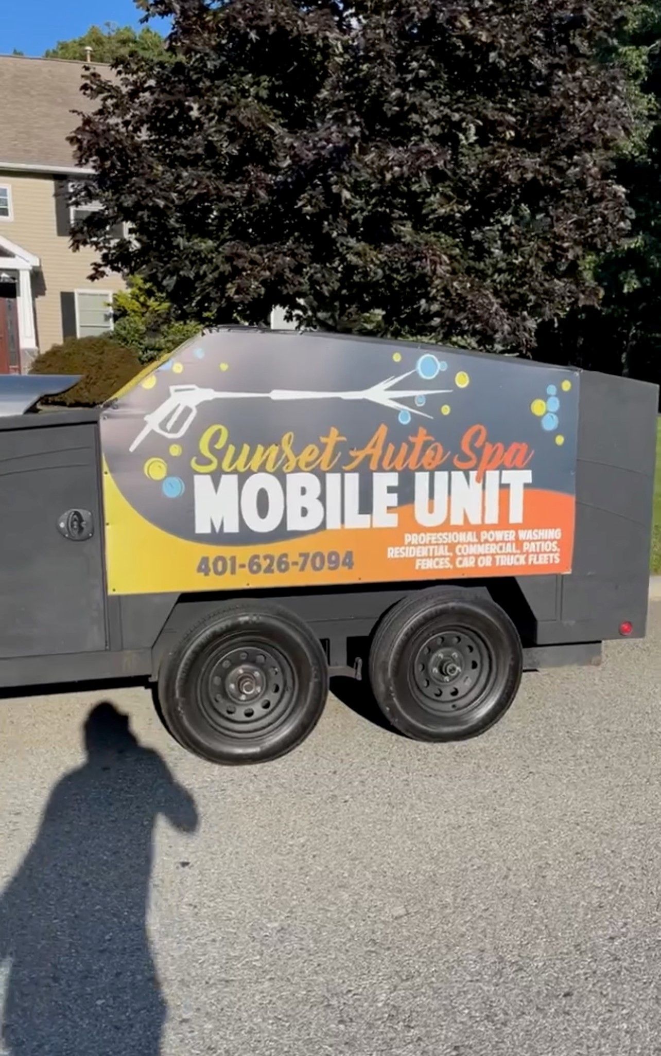 Mobile trailer for Sunset Auto Spa, with logo and phone number, parked on a street.