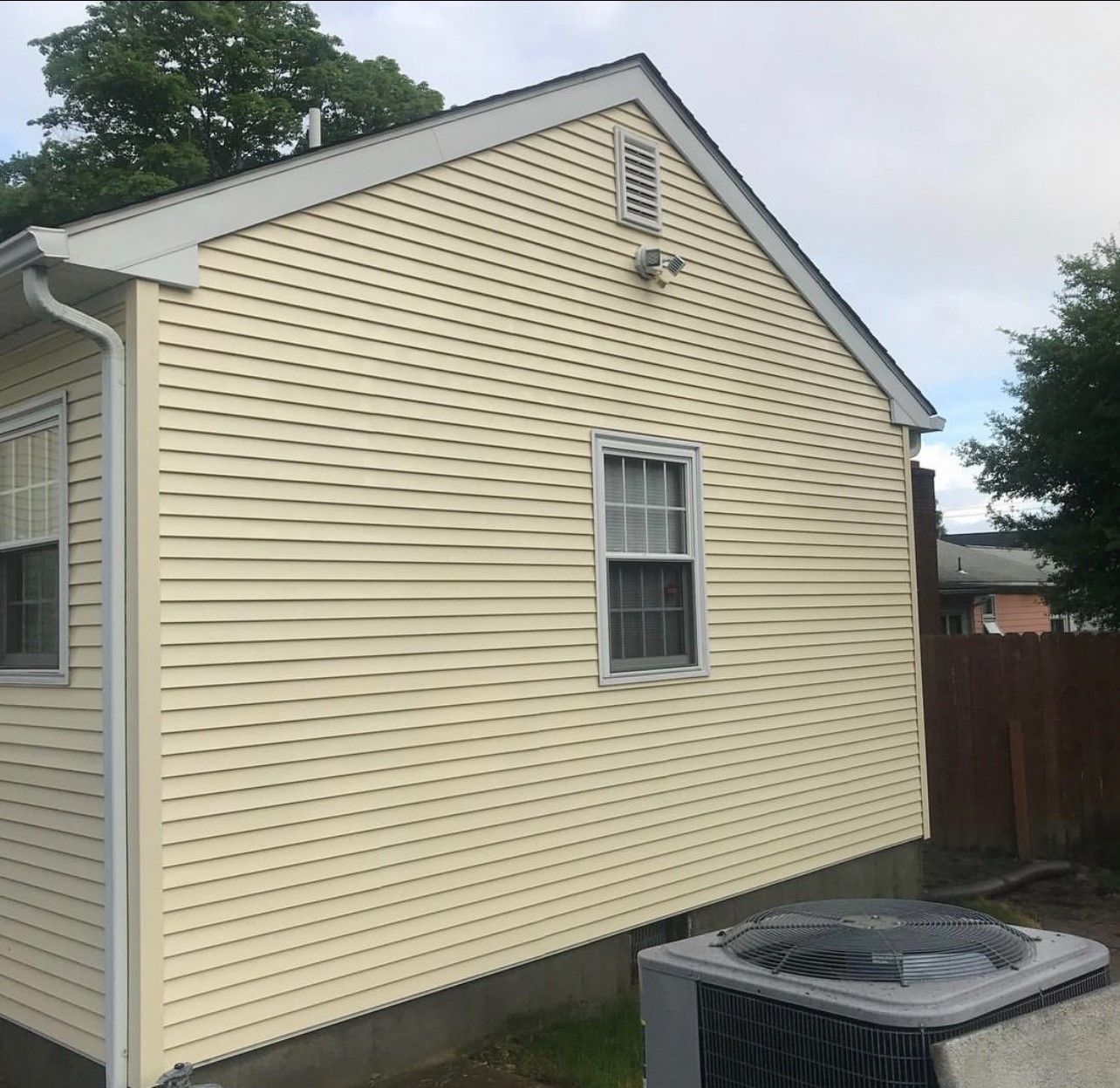 Yellow-sided house with white trim, a small window, and an AC unit outside.