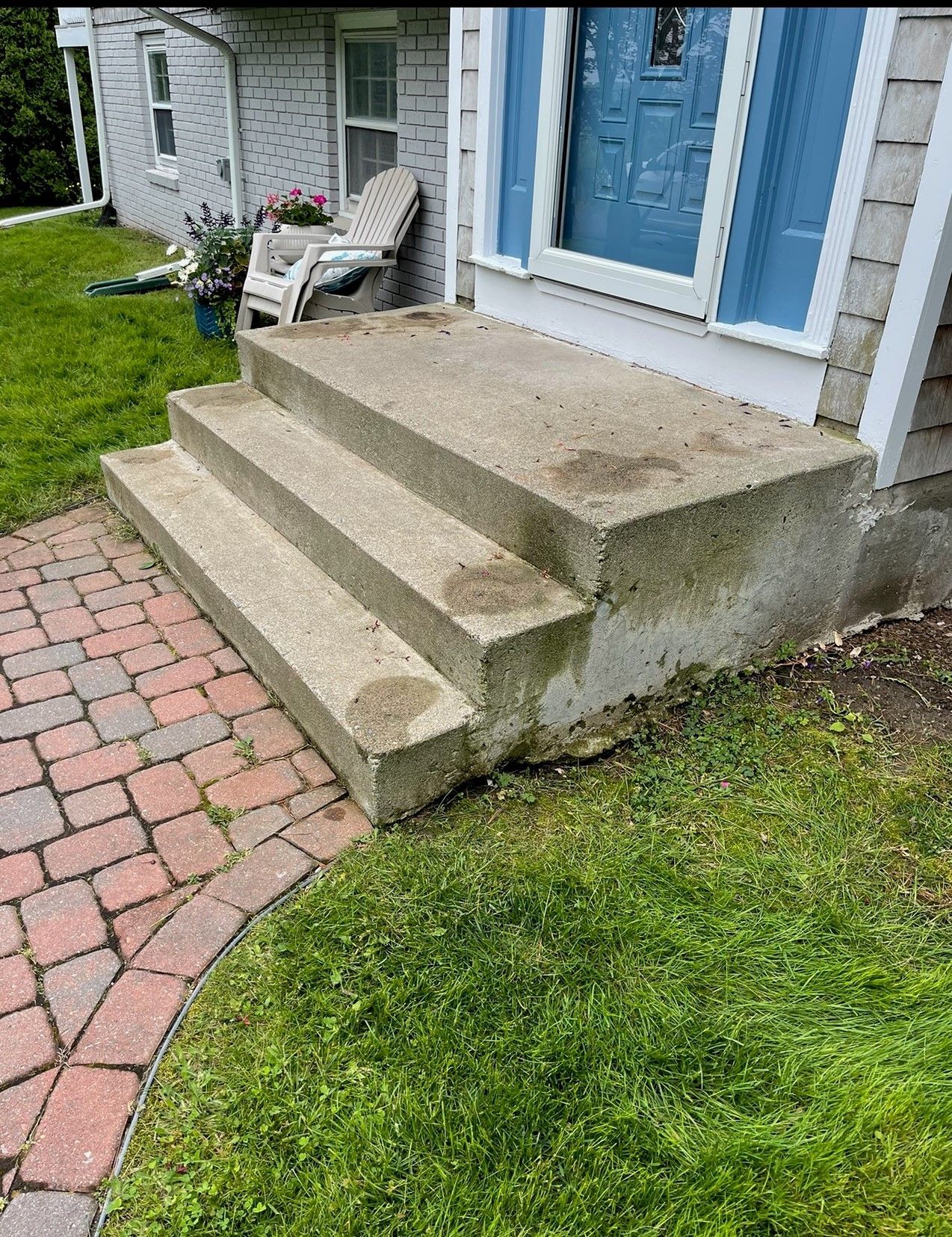 Concrete steps leading up to a blue door on a house with red brick walkway and green grass.