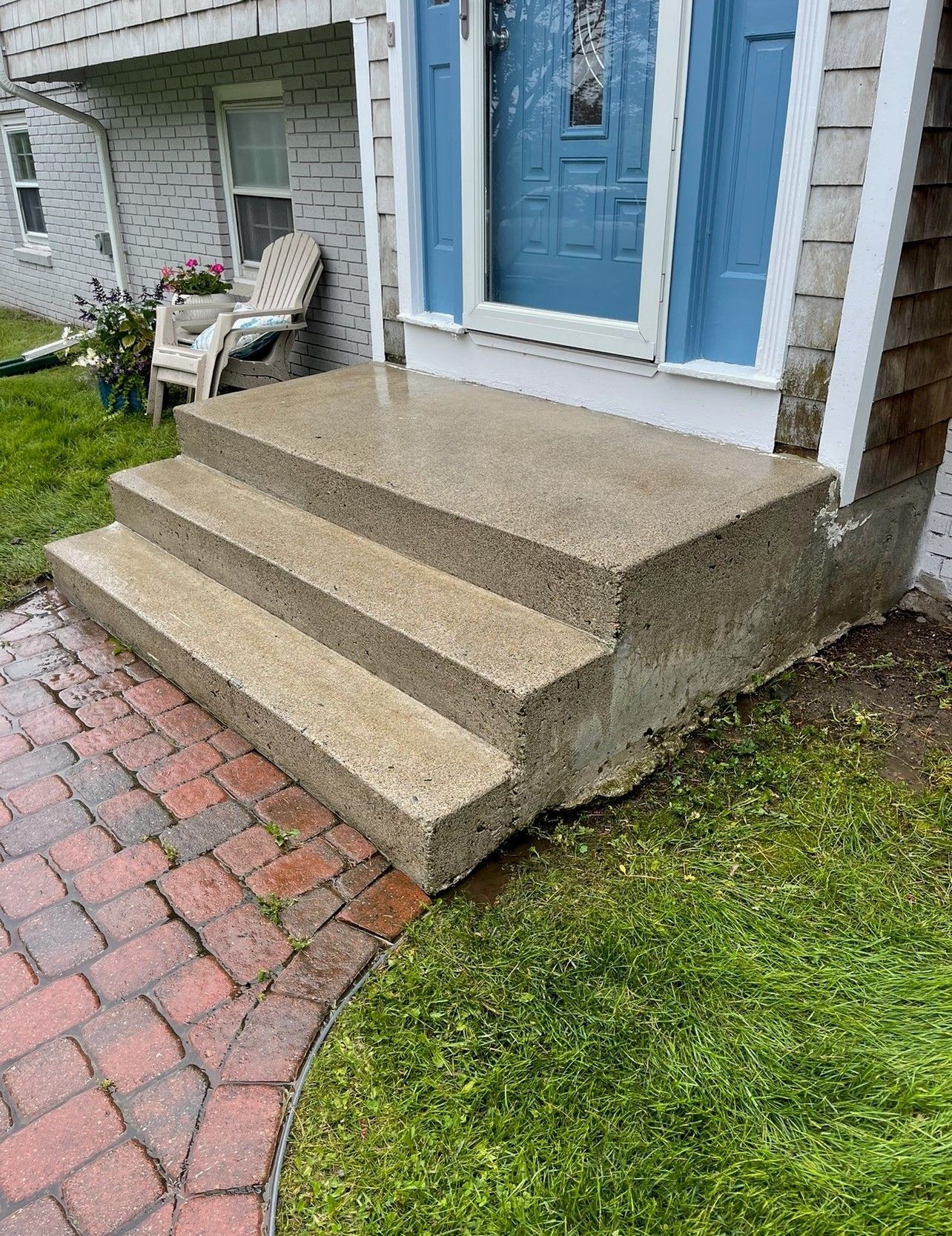 Concrete steps leading up to a house's blue door. Red brick path and green grass surround them.