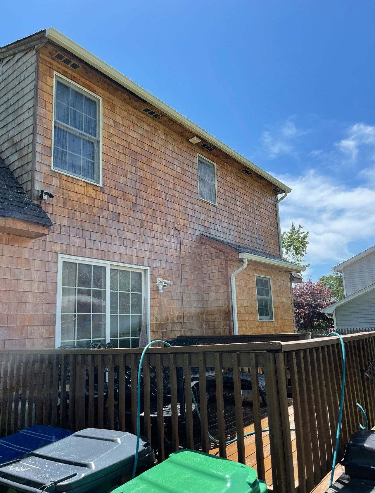 Side view of a two-story wooden shingle house with a deck. Blue sky overhead.