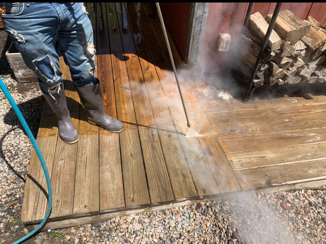 Person pressure washing a wooden deck, spraying water with vapor.