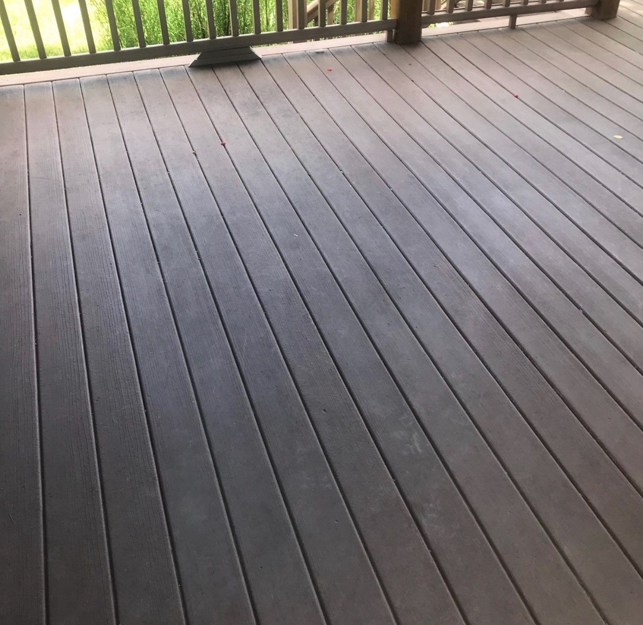 Dark brown wooden deck with railing in an outdoor setting.