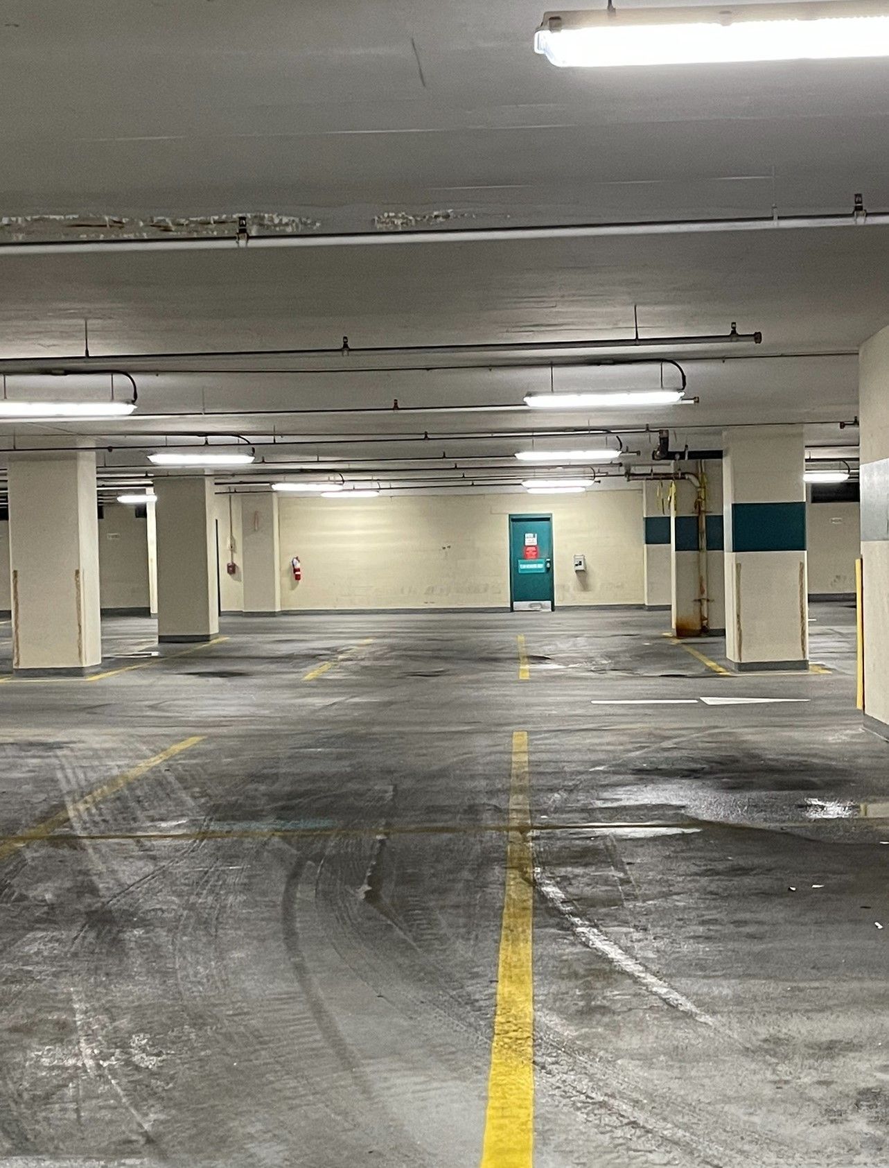 Empty parking garage with overhead lights and yellow lane markers. A blue door is visible at the far end.