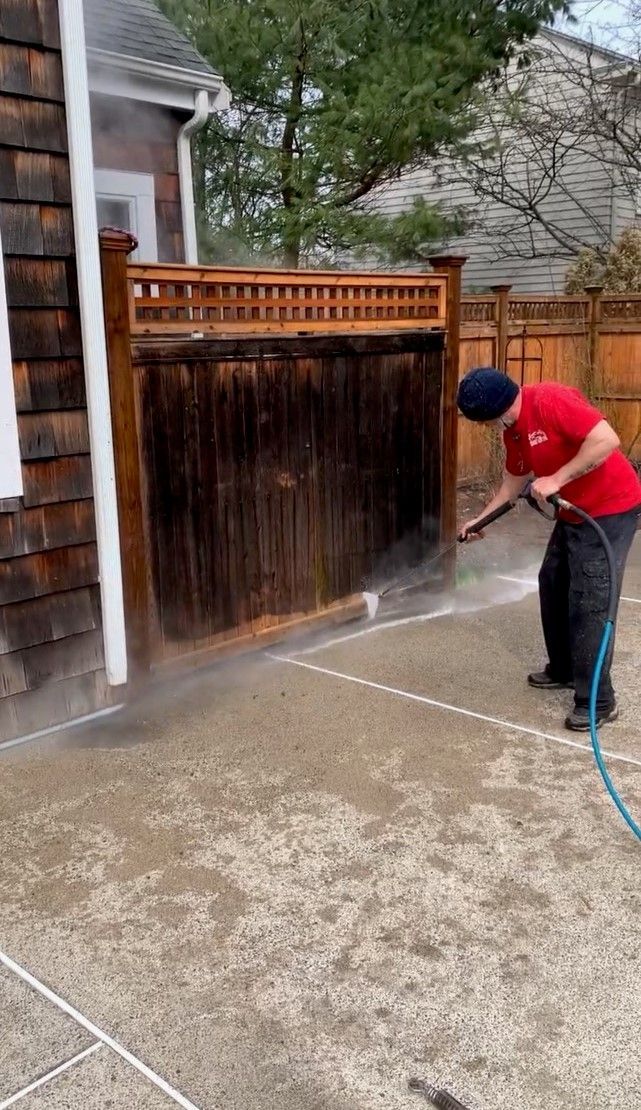 Person power washing a wooden fence and concrete patio.