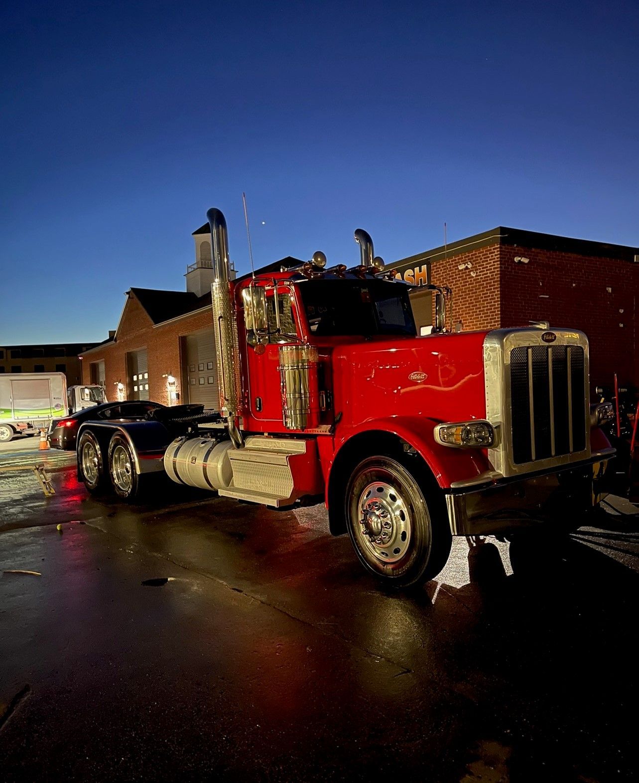 Red Peterbilt semi-truck parked in front of a brick building at dusk.