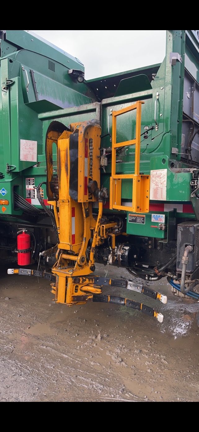 A green garbage truck with a yellow robotic arm, likely for automated trash collection.