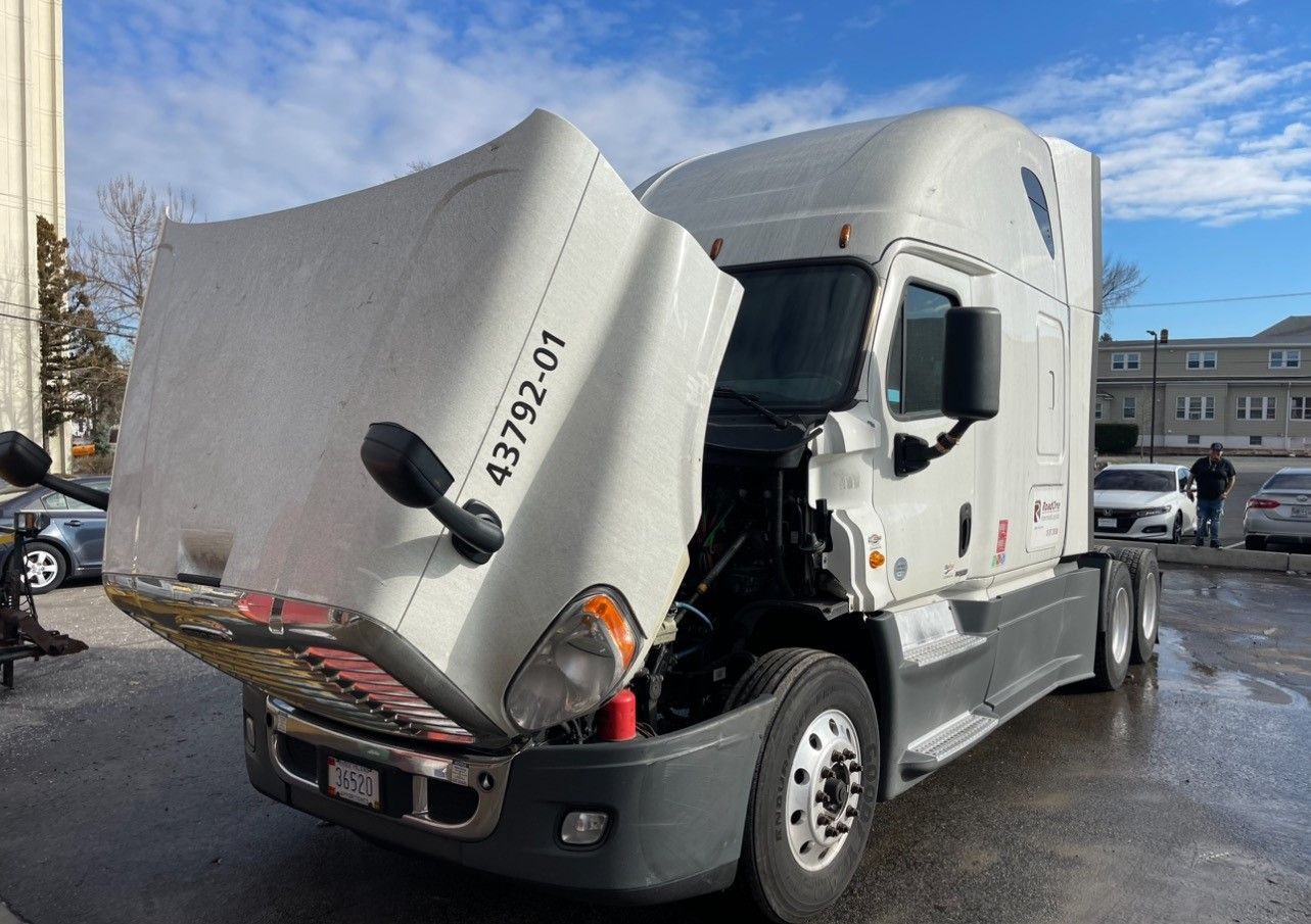 White semi-truck with open hood. Exterior shot on a street, overcast day.