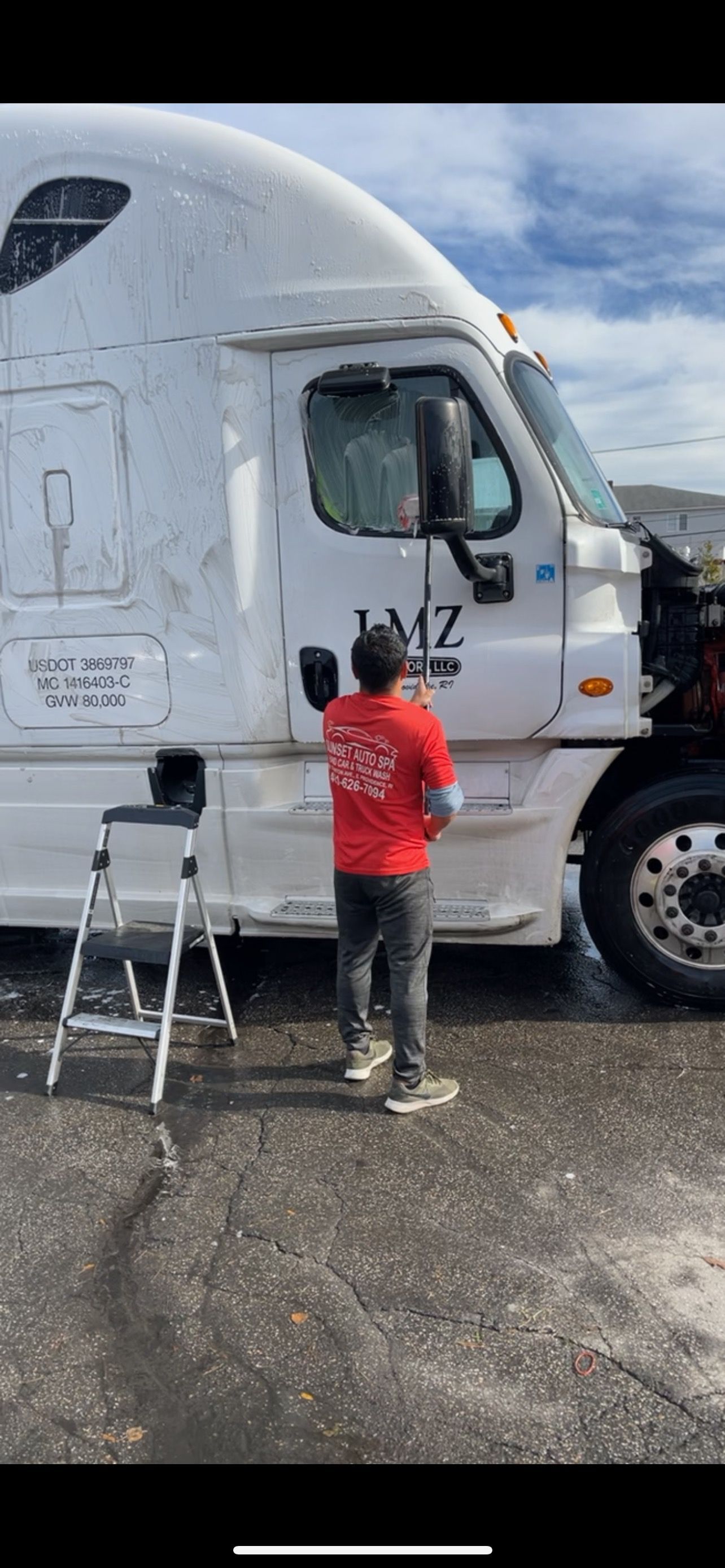 Person washes white semi-truck with a ladder on an overcast day.