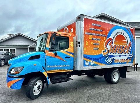Box truck with colorful sunset-themed graphics parked in front of a building.