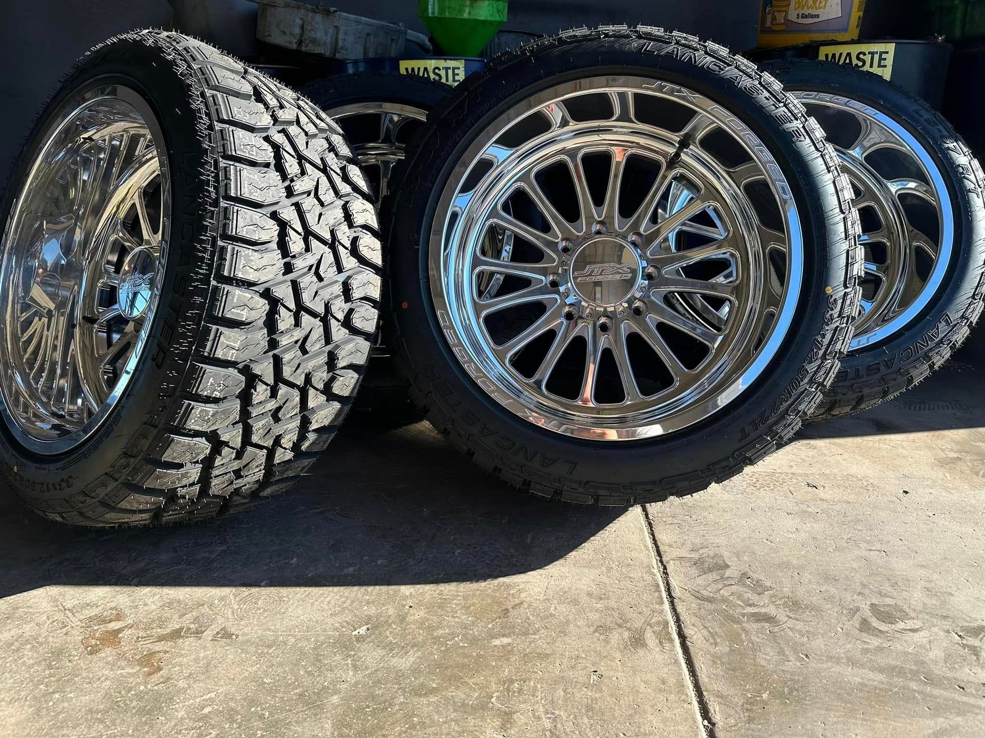 A cluster of chrome-finished multi-spoke truck wheels with aggressive tread tires sitting on a concrete surface.