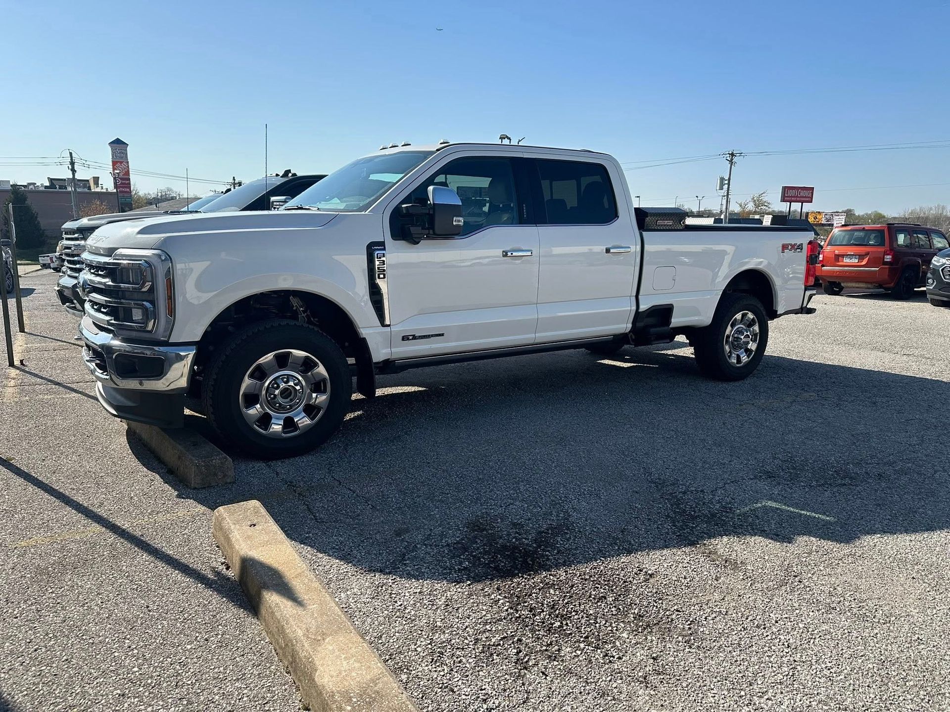 A white Ford F-Series crew cab pickup truck parked on a gravel car dealership lot under a clear blue sky.