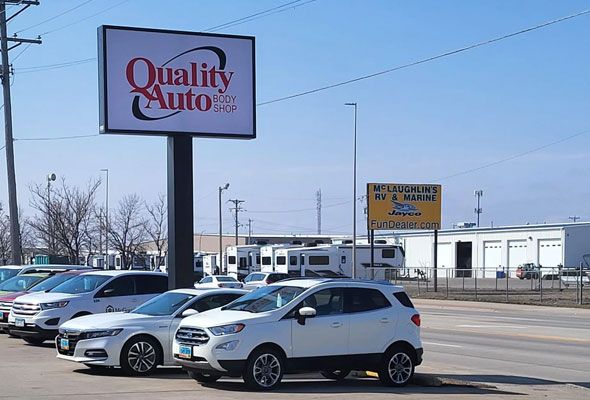 A row of cars are parked in front of a quality auto sign.