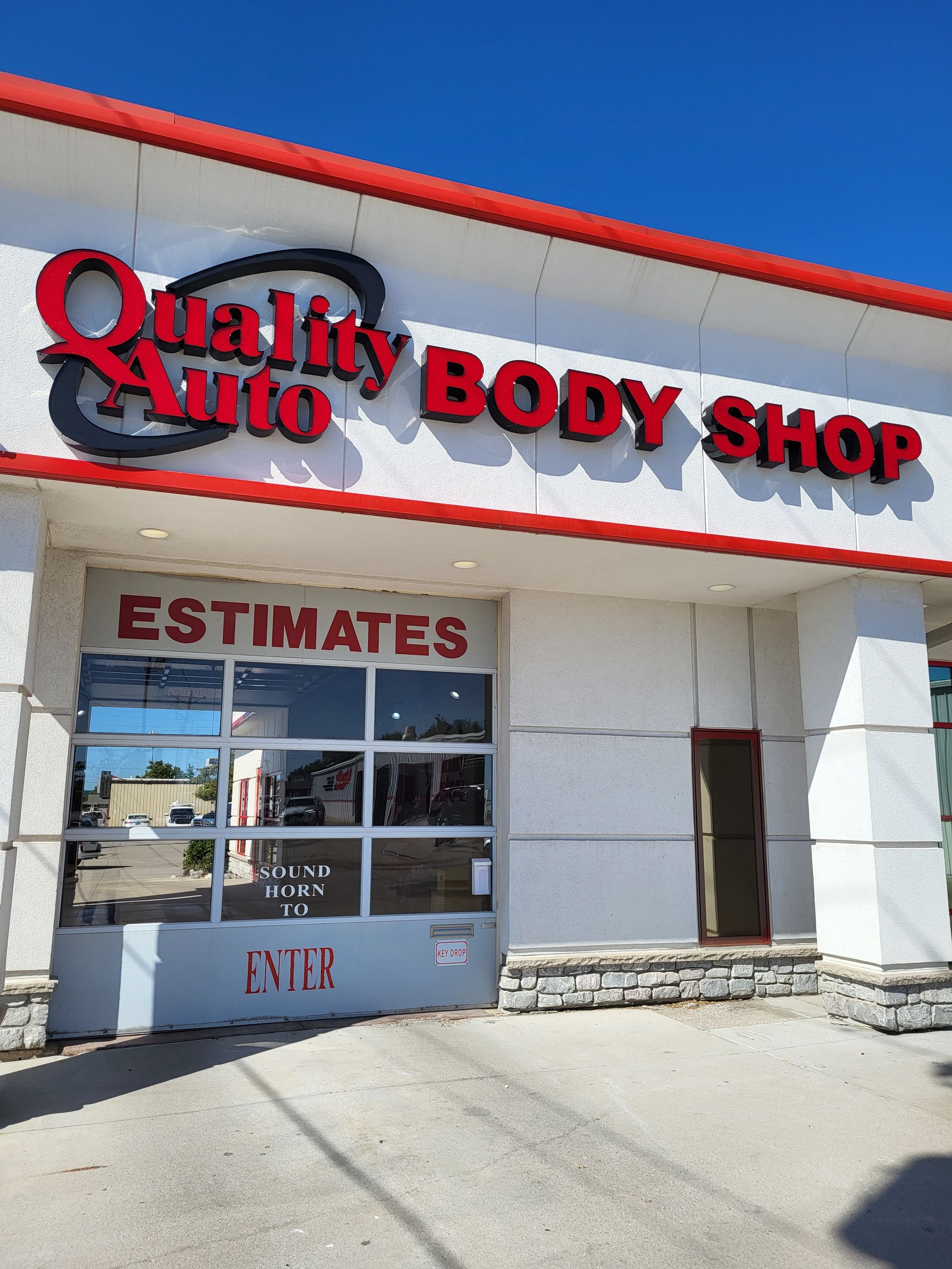 A white building with a red sign that says Quality Auto Body Shop